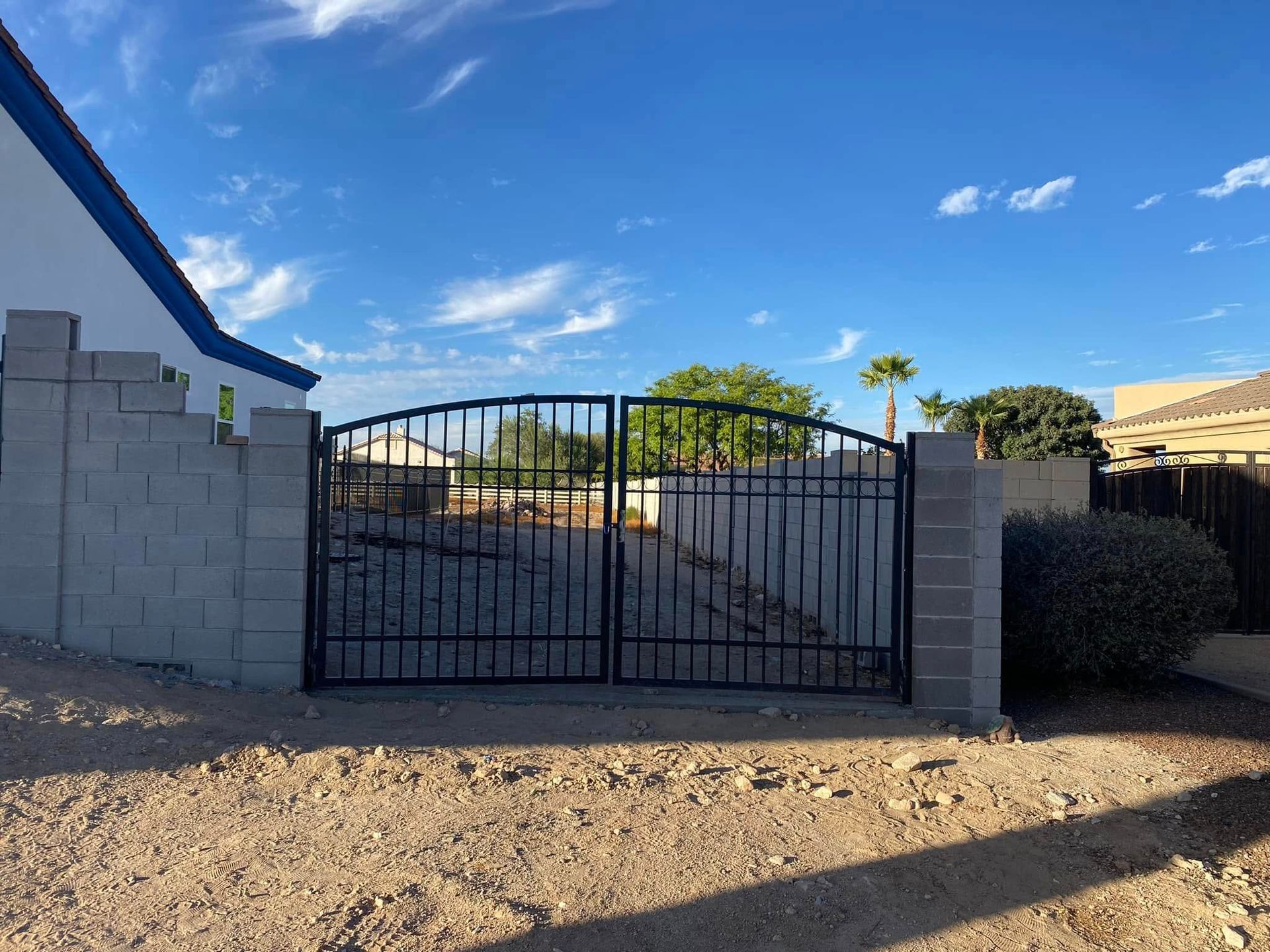 Black metal driveway gate between gray block walls in a sunny desert yard