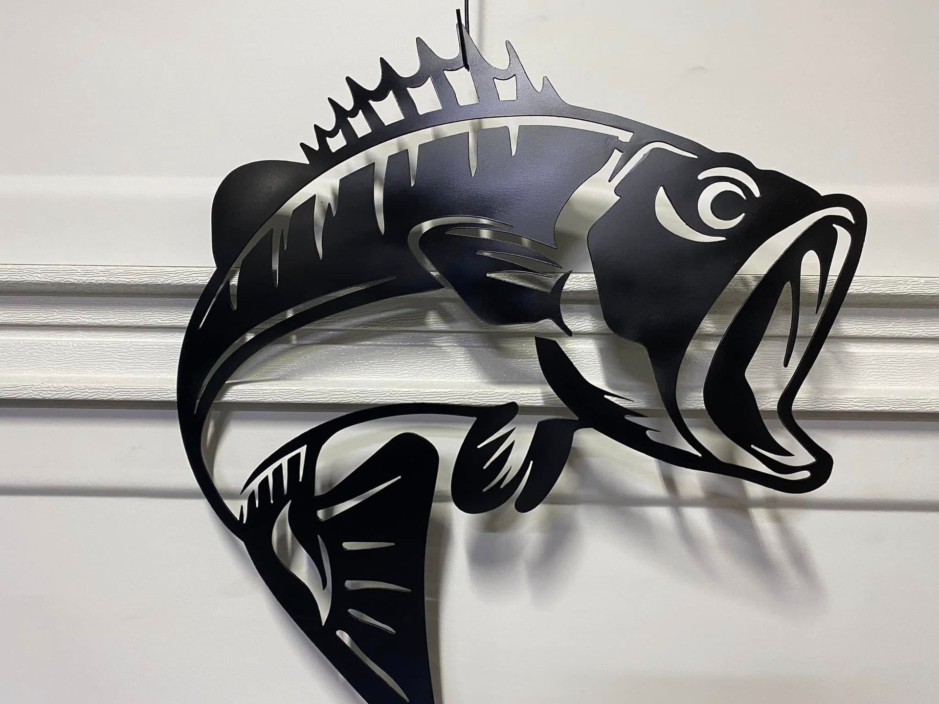 Black metal fish wall sculpture with open mouth and spiky fins on a light wall