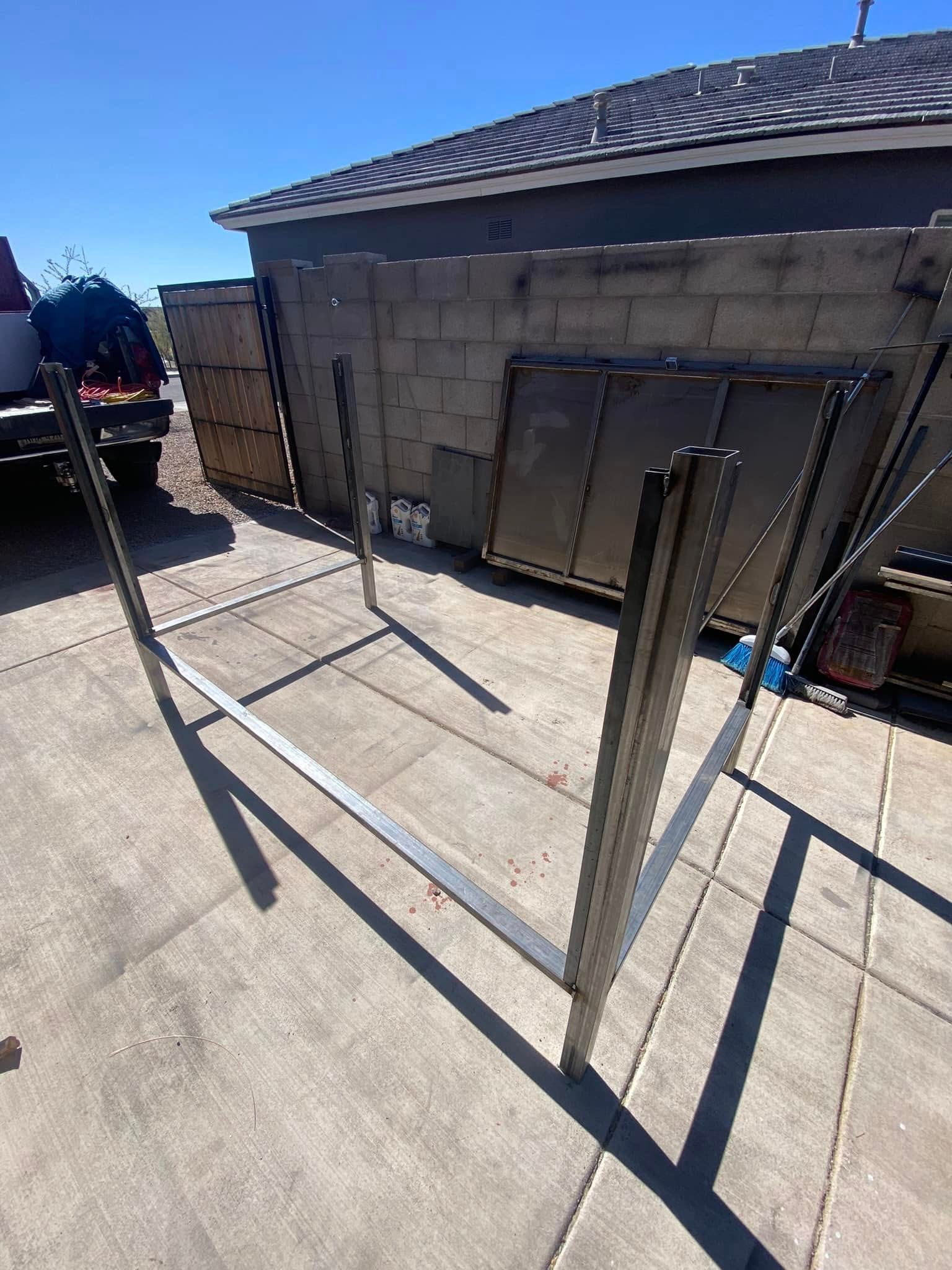Outdoor patio with concrete slabs, metal posts, and a garage wall under bright sunlight.