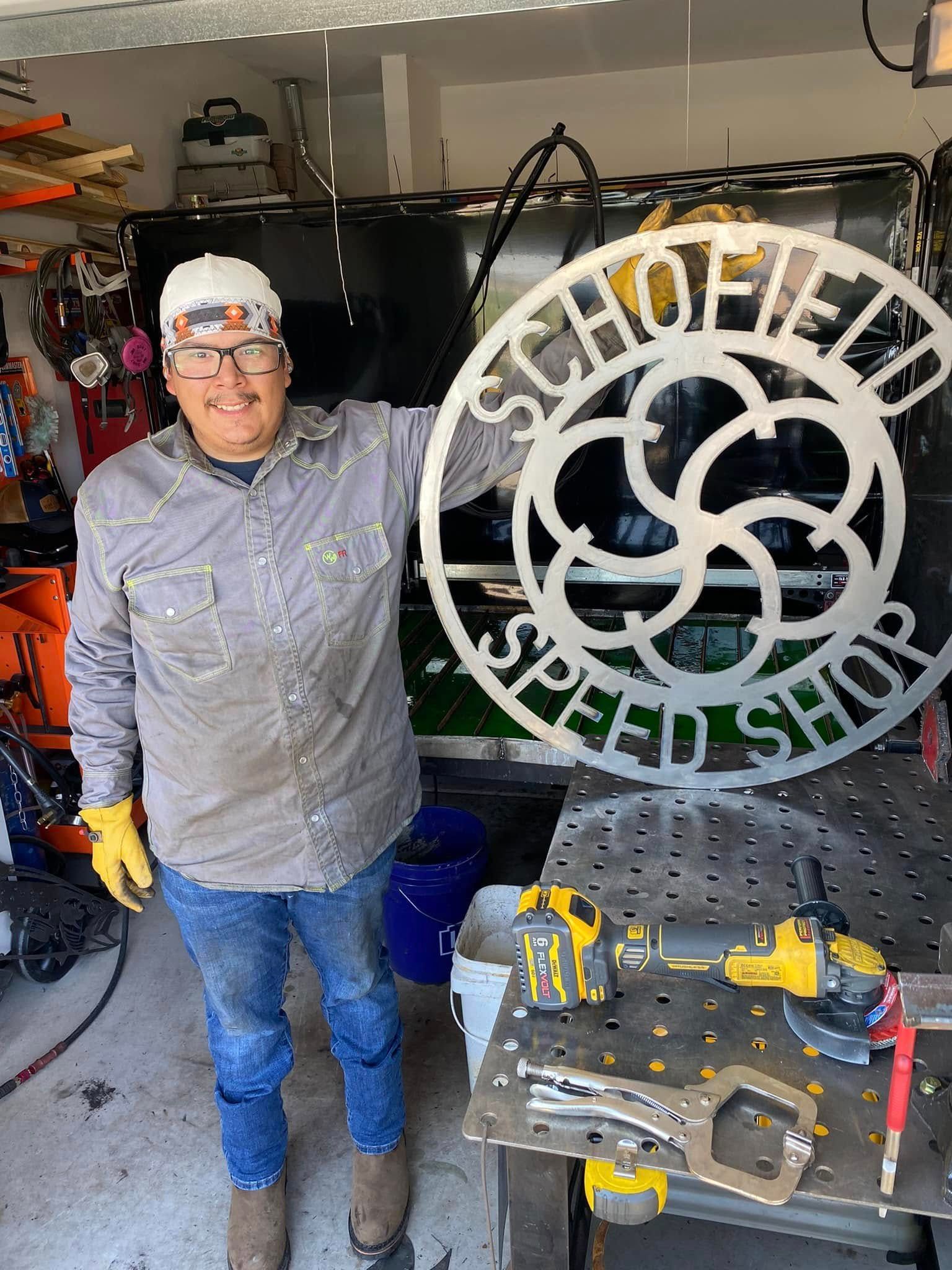 Person in a garage workshop beside a large circular metal sign, wearing gloves and safety glasses.
