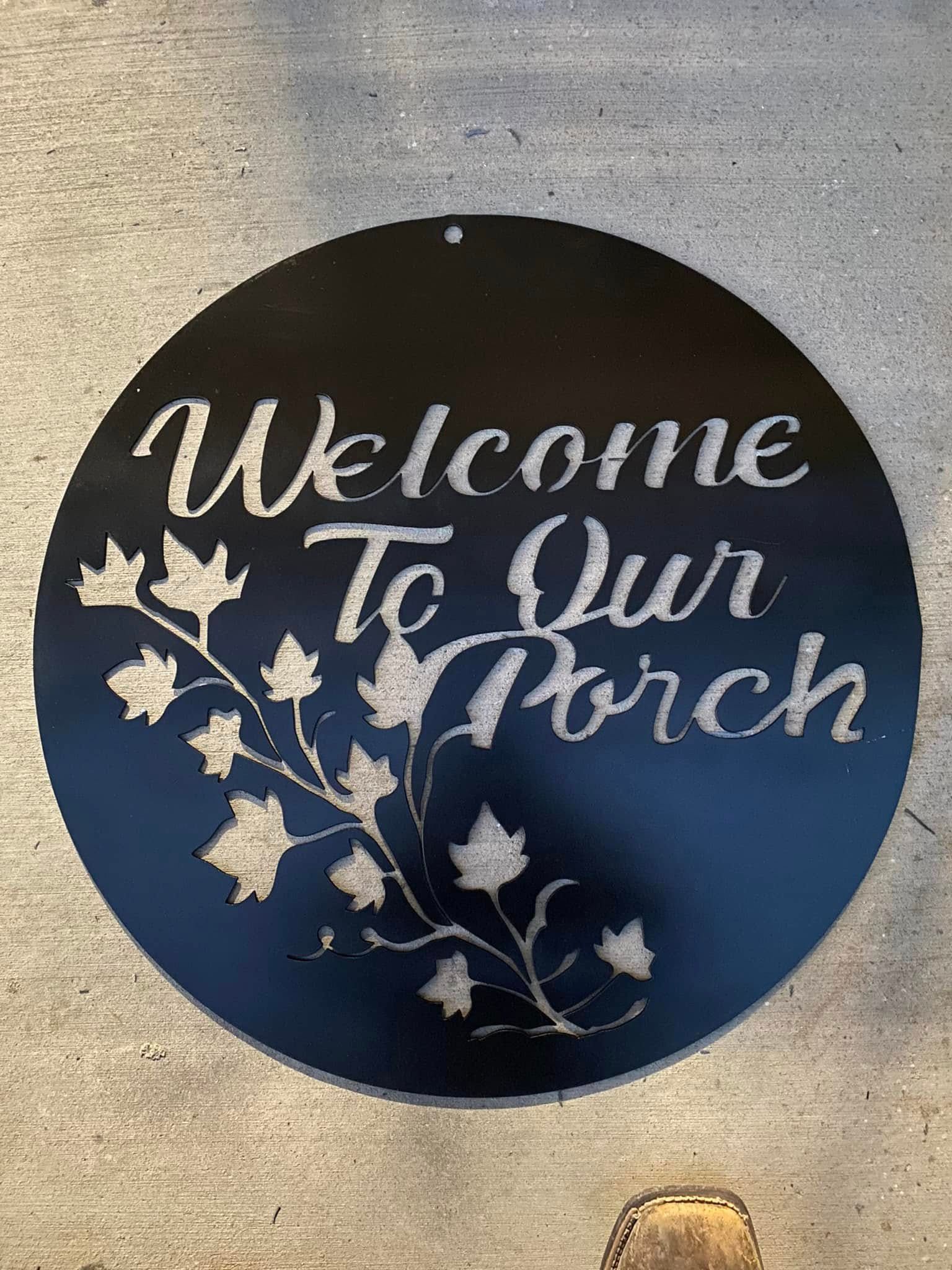 Black round sign on a wall reads “Welcome To Your Porch” with white leaf branches.