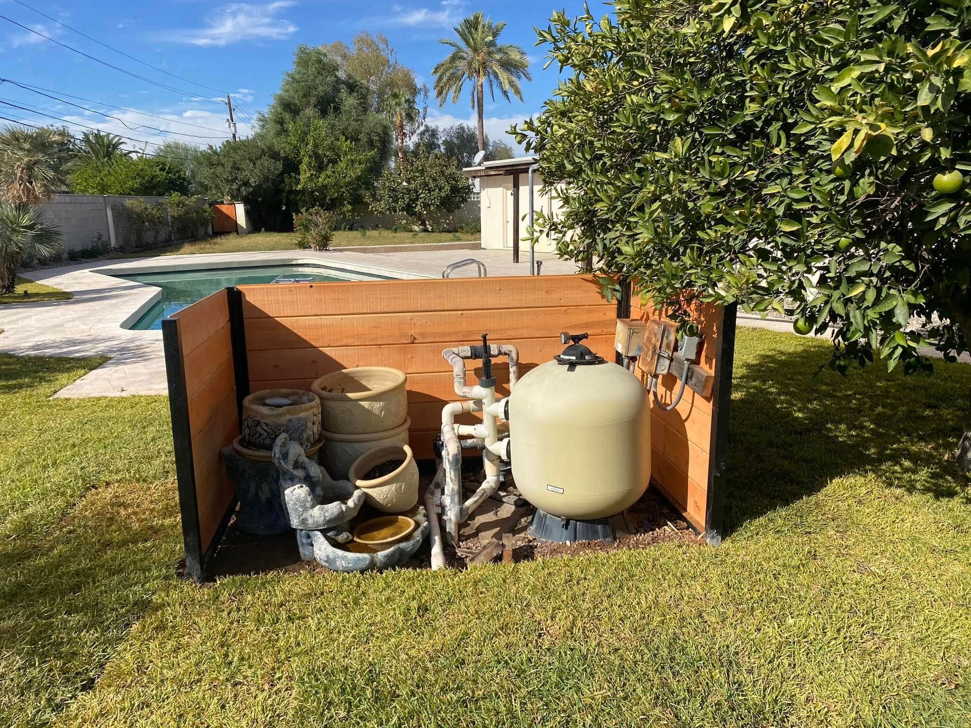 Outdoor pool equipment area with pipes, tanks, and a propane tank beside a yard and swimming pool