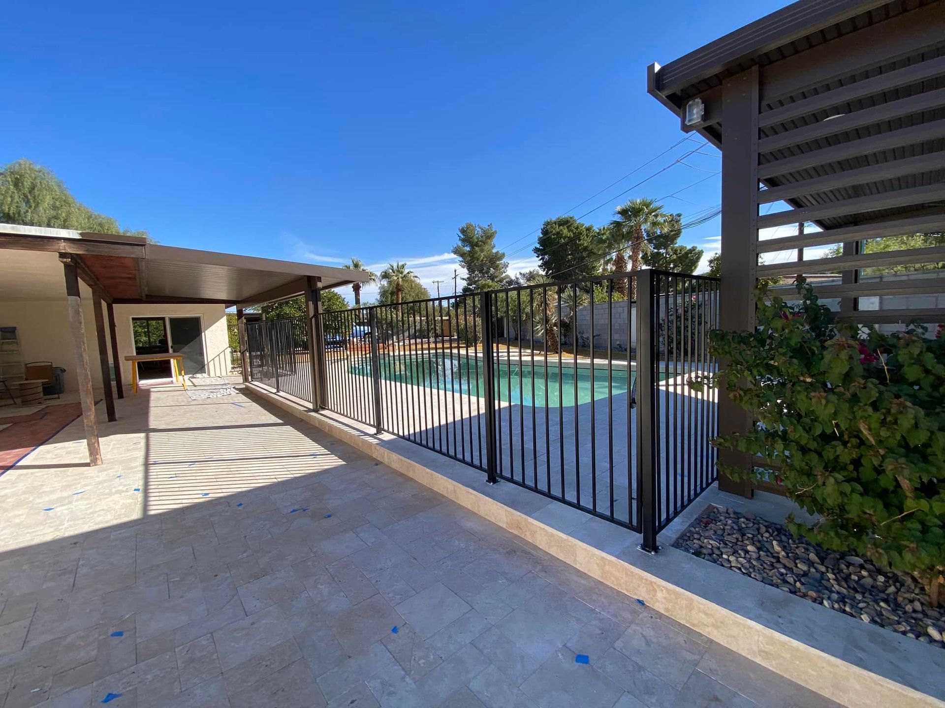 Patio with black fence beside a swimming pool under a clear blue sky