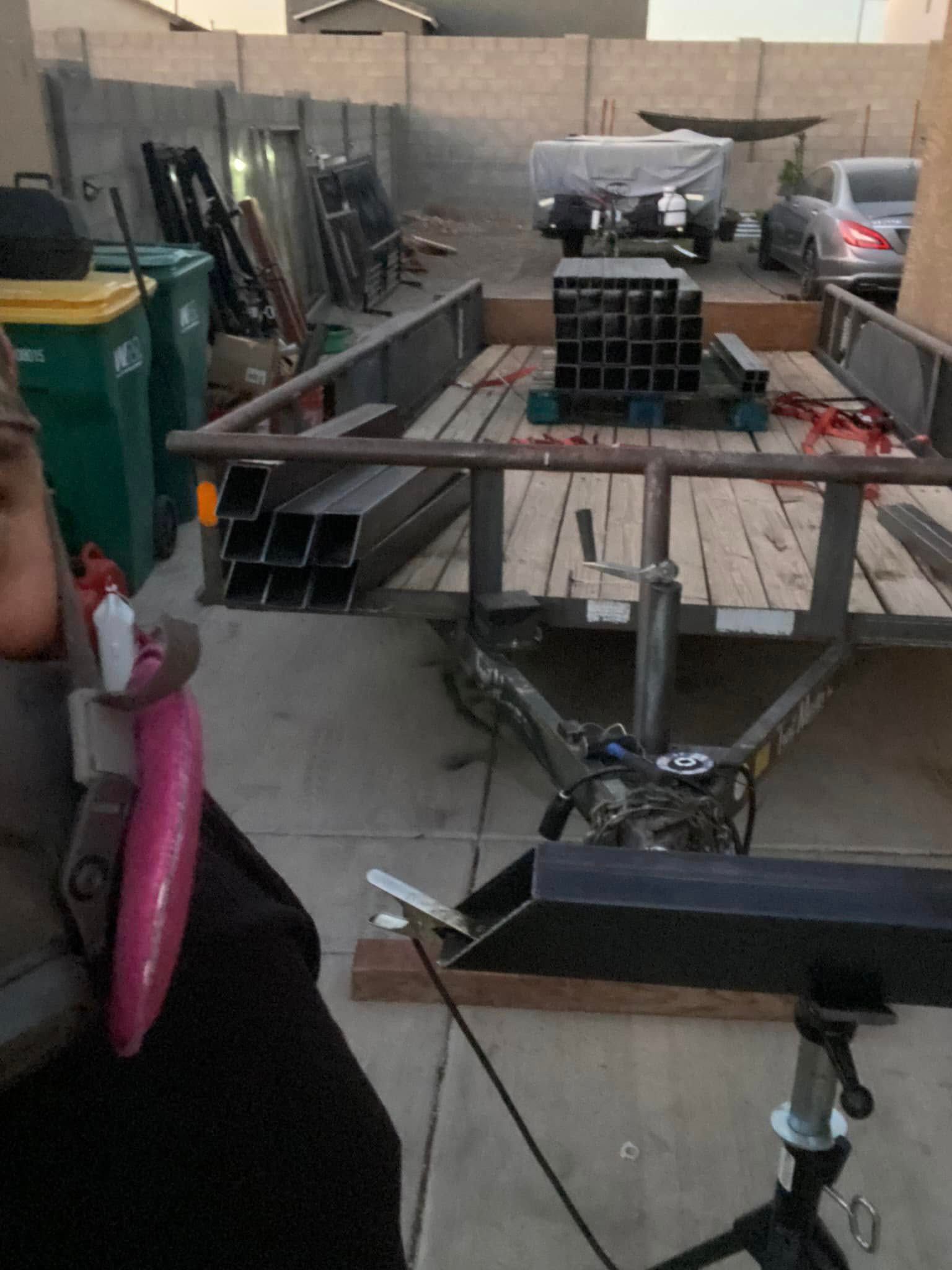 Outdoor workshop table with metal parts, a person at left, and tools in a concrete yard