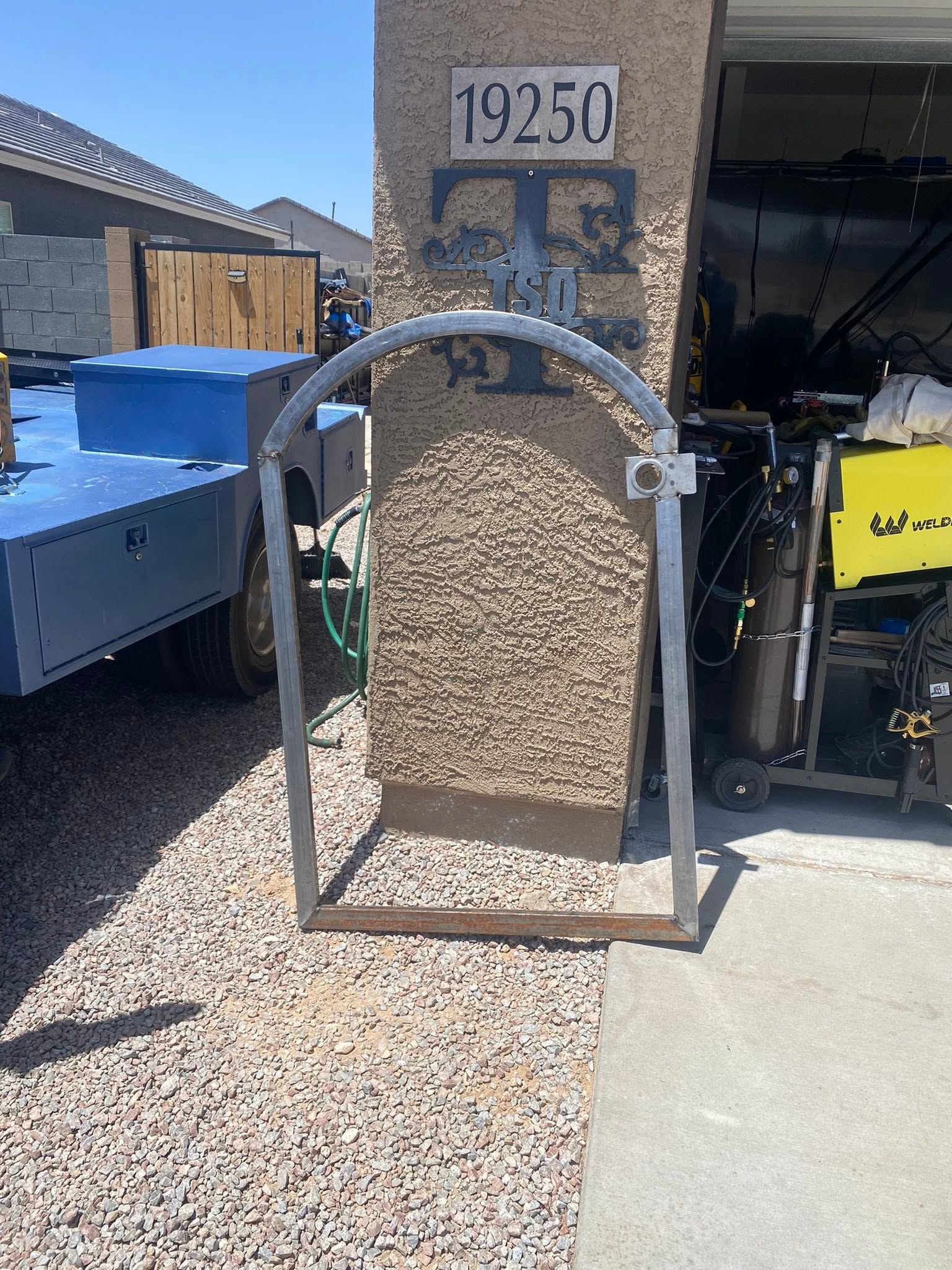 Stone plaque with arched metal frame and number 19250 beside a blue dumpster in a gravel yard