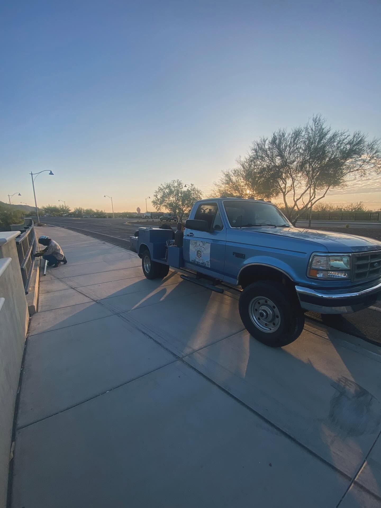 Blue pickup truck parked on a driveway at sunset, with a trailer hitch and desert landscape in the background