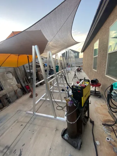 Outdoor patio worksite with shade sails, ladders, tools, and equipment between two buildings