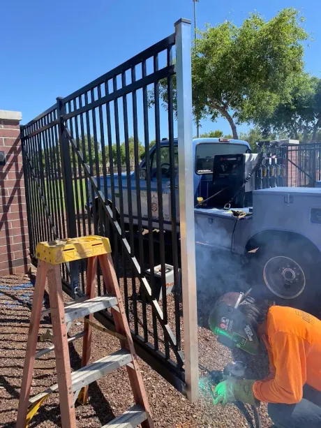 Man welding a black metal gate beside a truck, with smoke rising in a sunny yard.