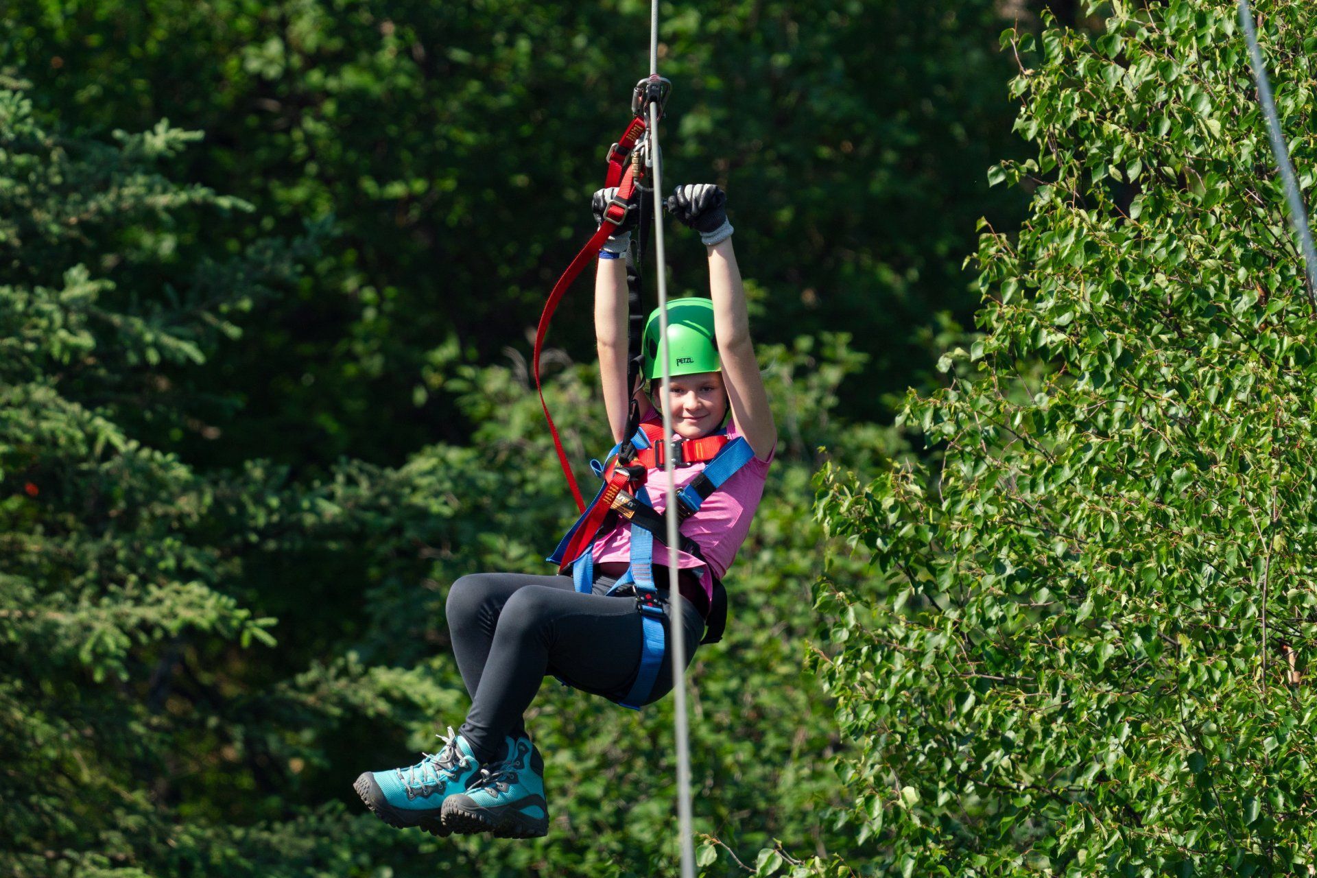 Person ziplining through a forest, wearing a green helmet and pink jacket