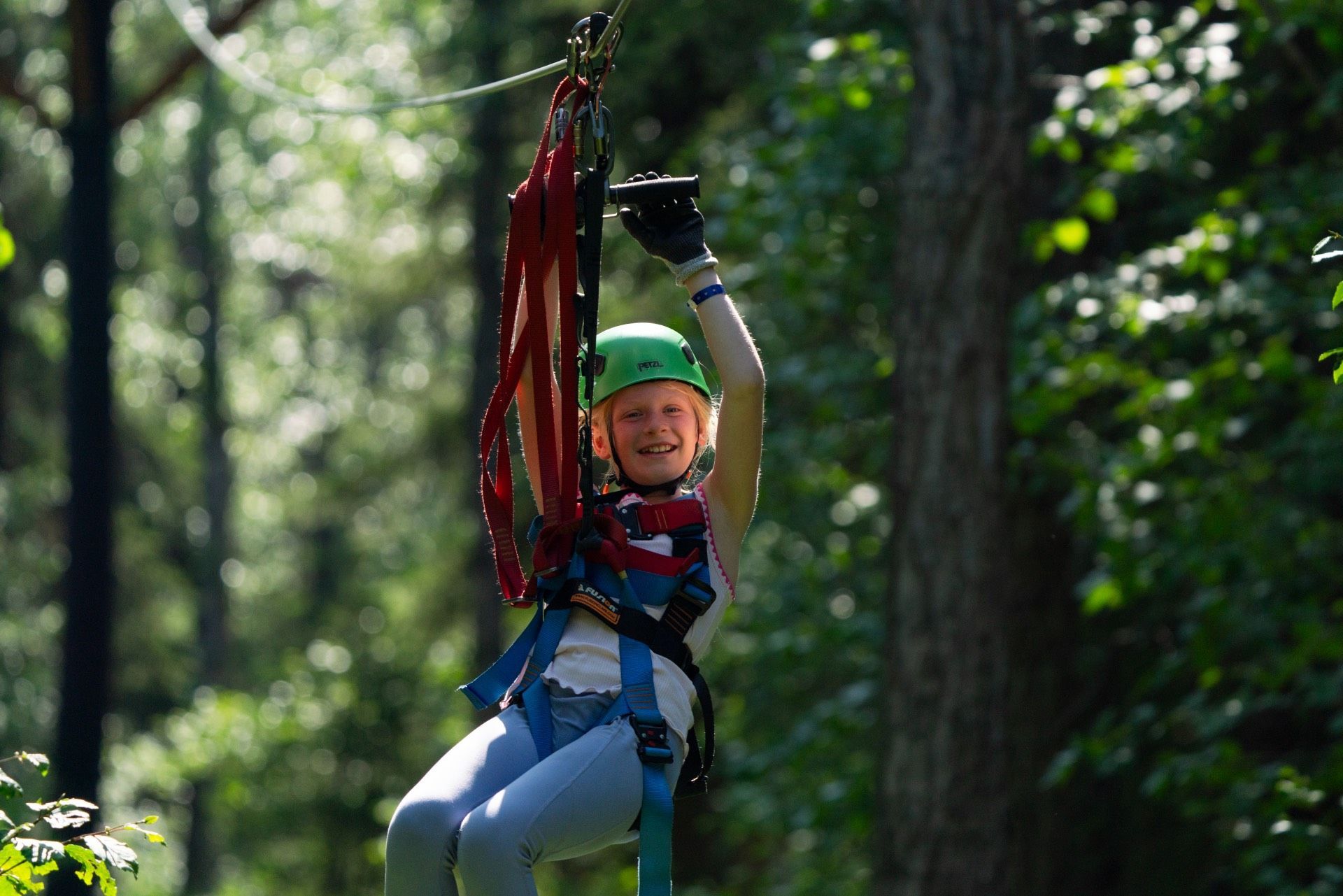 Person wearing a green helmet zip-lining through a forest on a sunny day