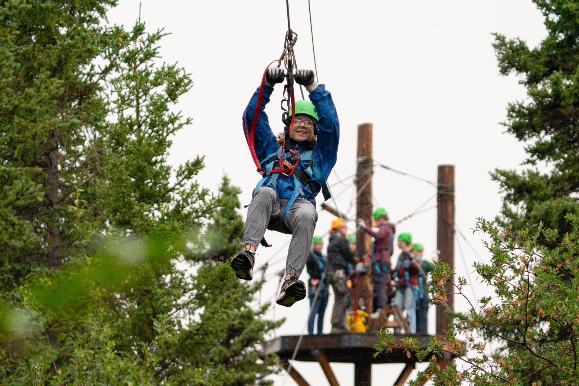 Person zip-lining between trees while a group watches from a platform behind.