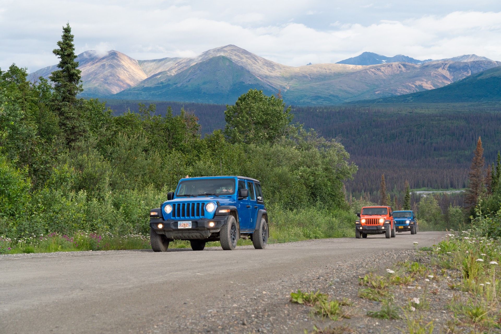 Blue Jeep and orange SUV driving on a gravel road with mountains in the background