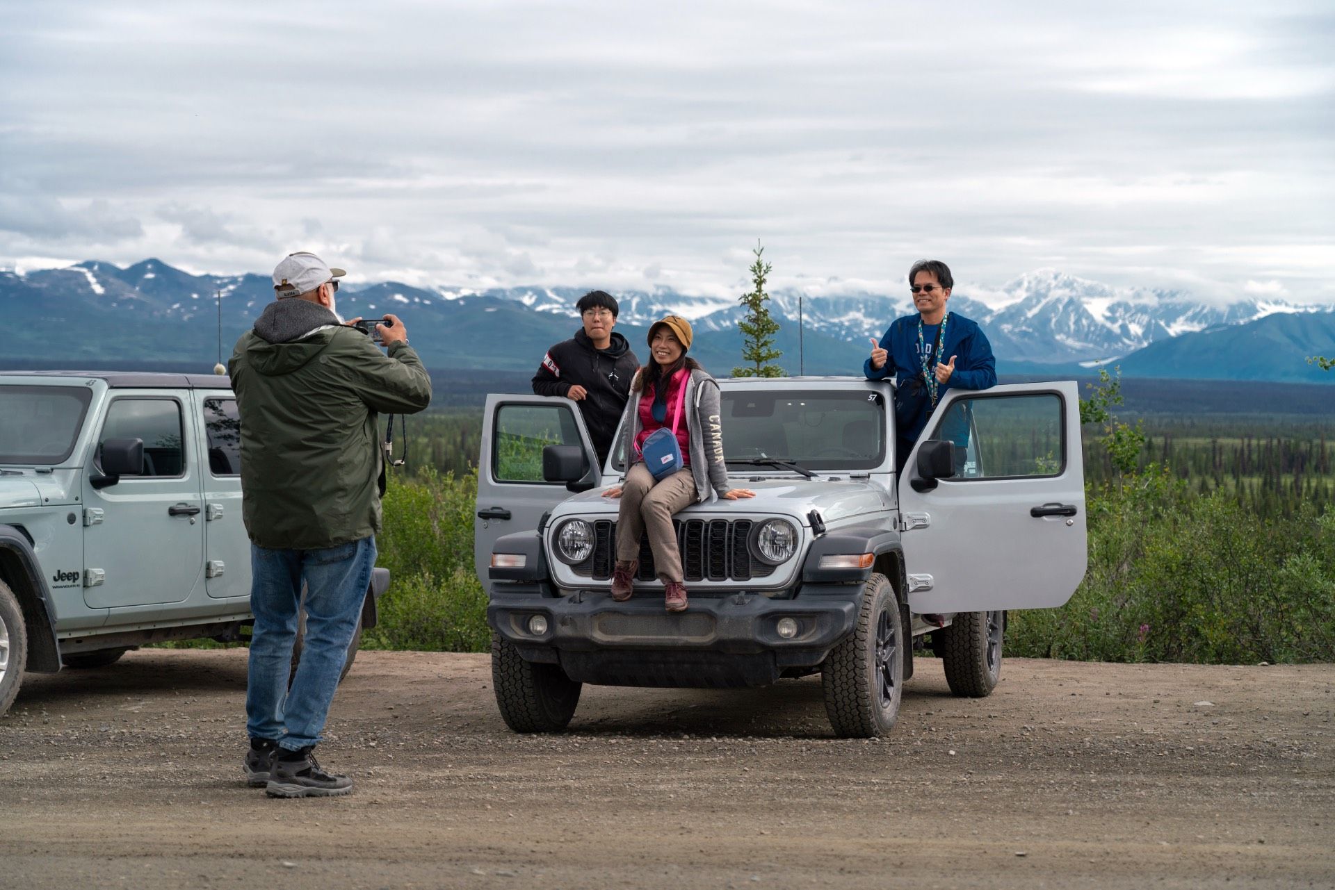 People posing on and around a white Jeep with mountains in the background