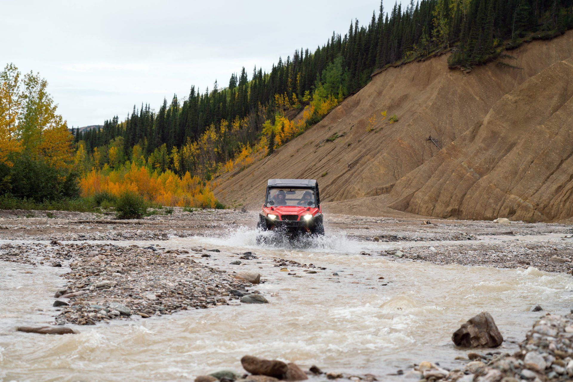 Off-road vehicle driving through a shallow muddy river near a forested hillside