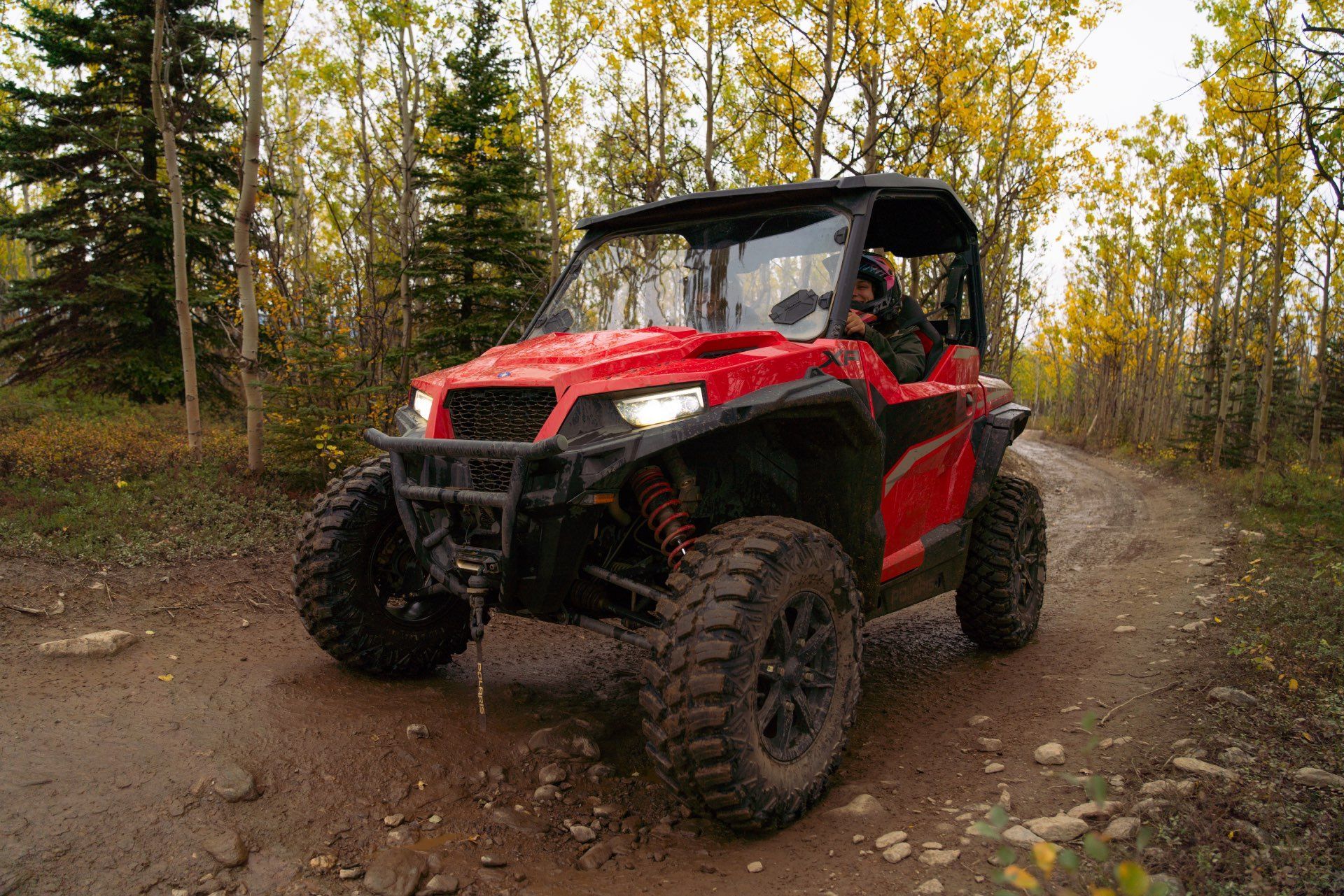 Red off-road ATV driving on a muddy forest trail with autumn trees nearby