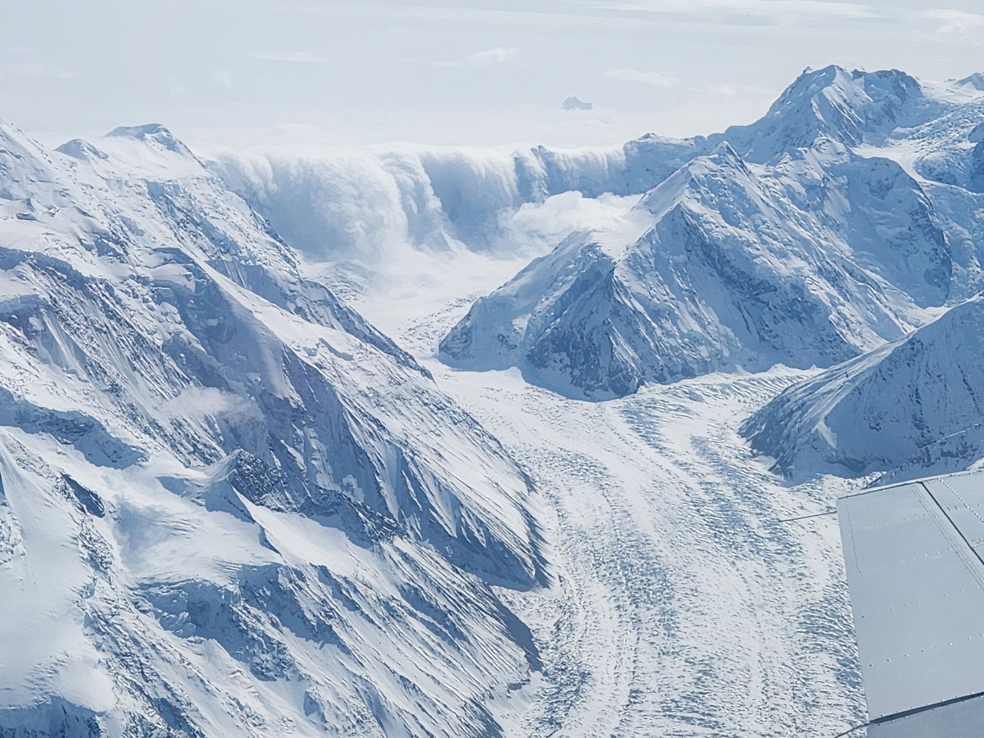 Snow-covered mountain range with a glacier under a pale blue sky