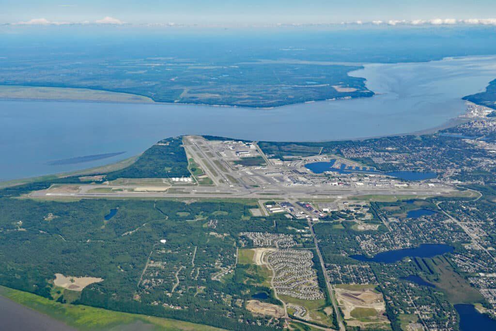 Aerial view of a coastal city with a narrow peninsula, harbor waters, and dense green neighborhoods