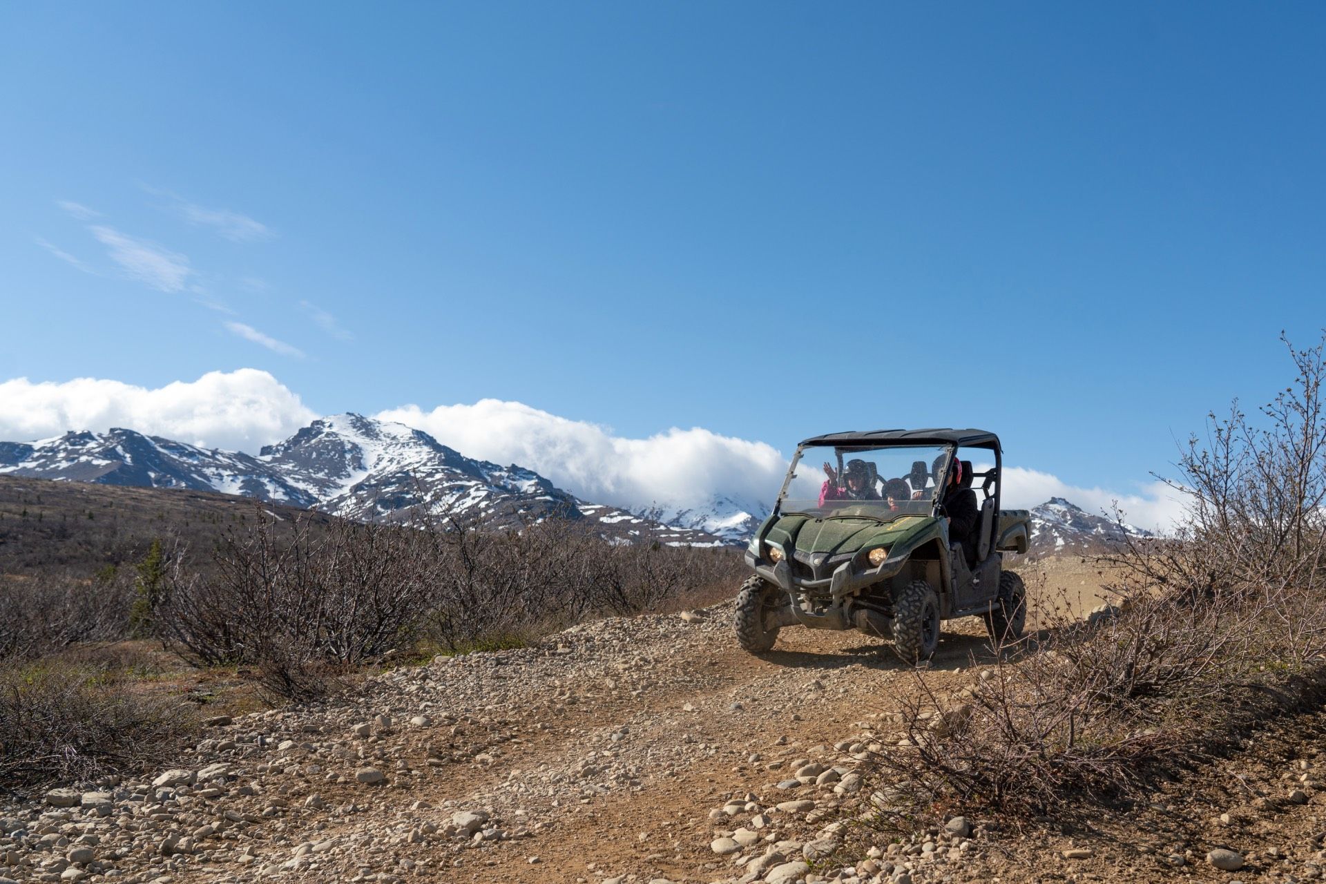 Off-road vehicle on a dirt trail with snowcapped mountains under a blue sky