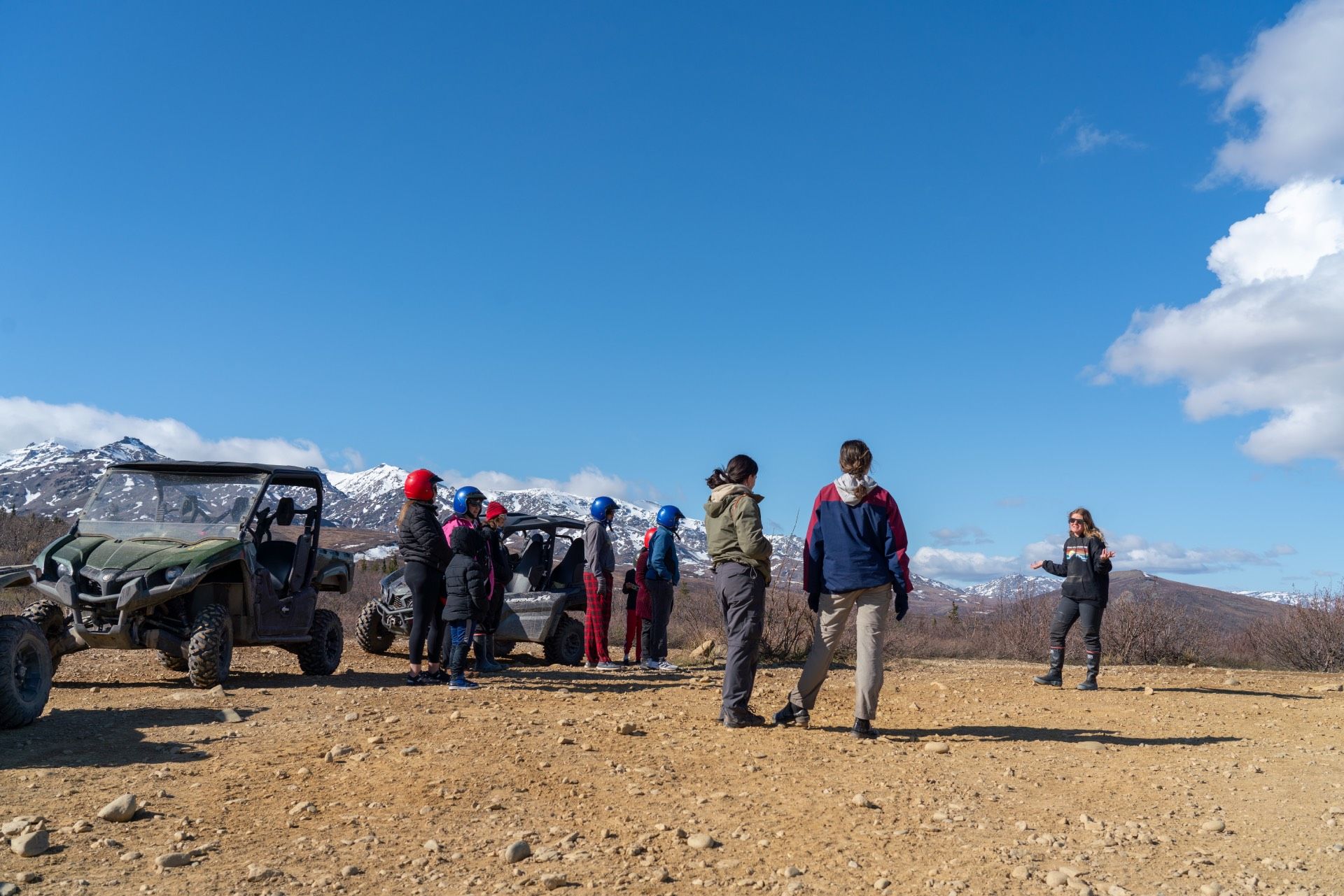 People standing near off-road vehicles on a rocky mountain plateau under a blue sky.