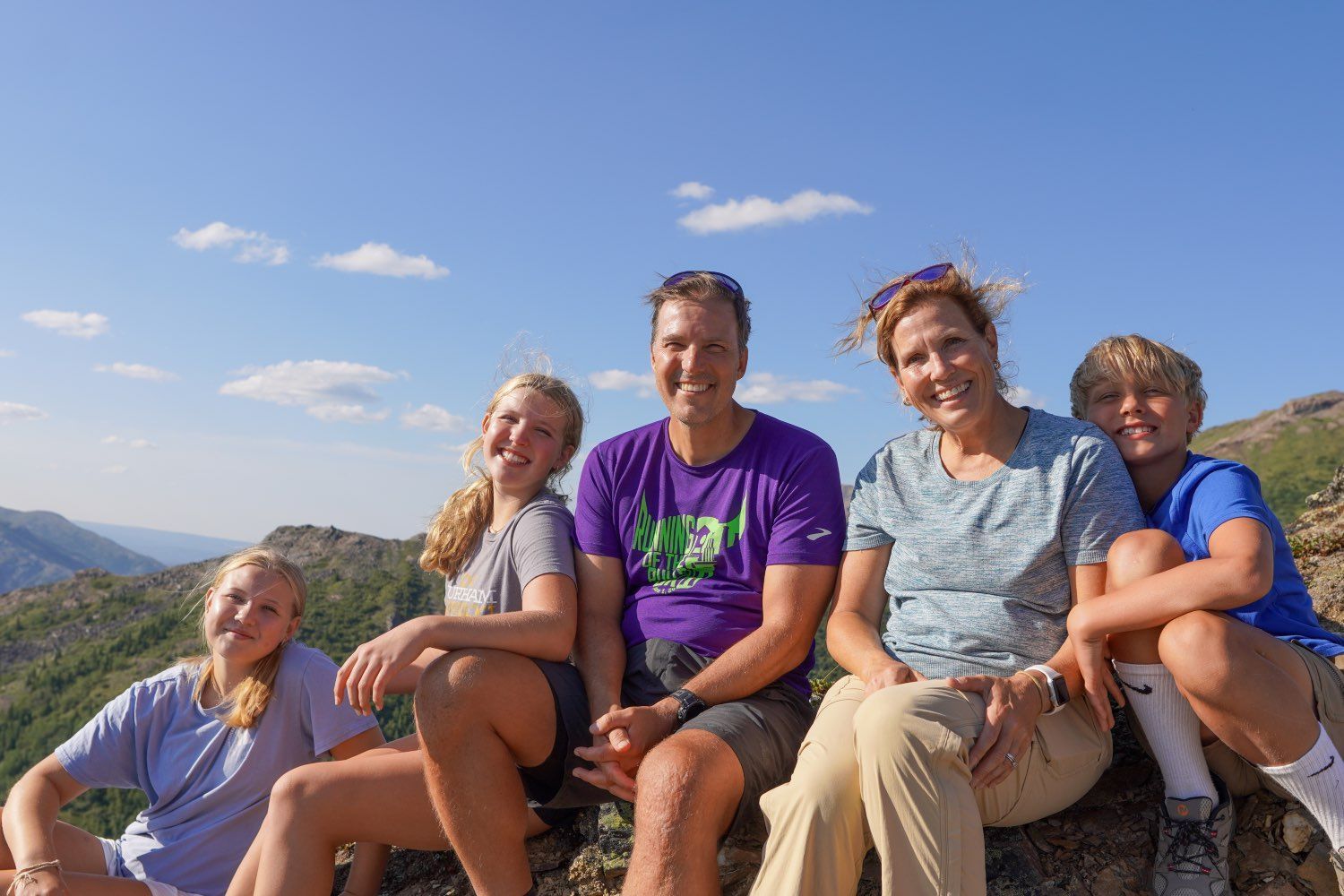 Five people smiling on a mountain overlook under a bright blue sky