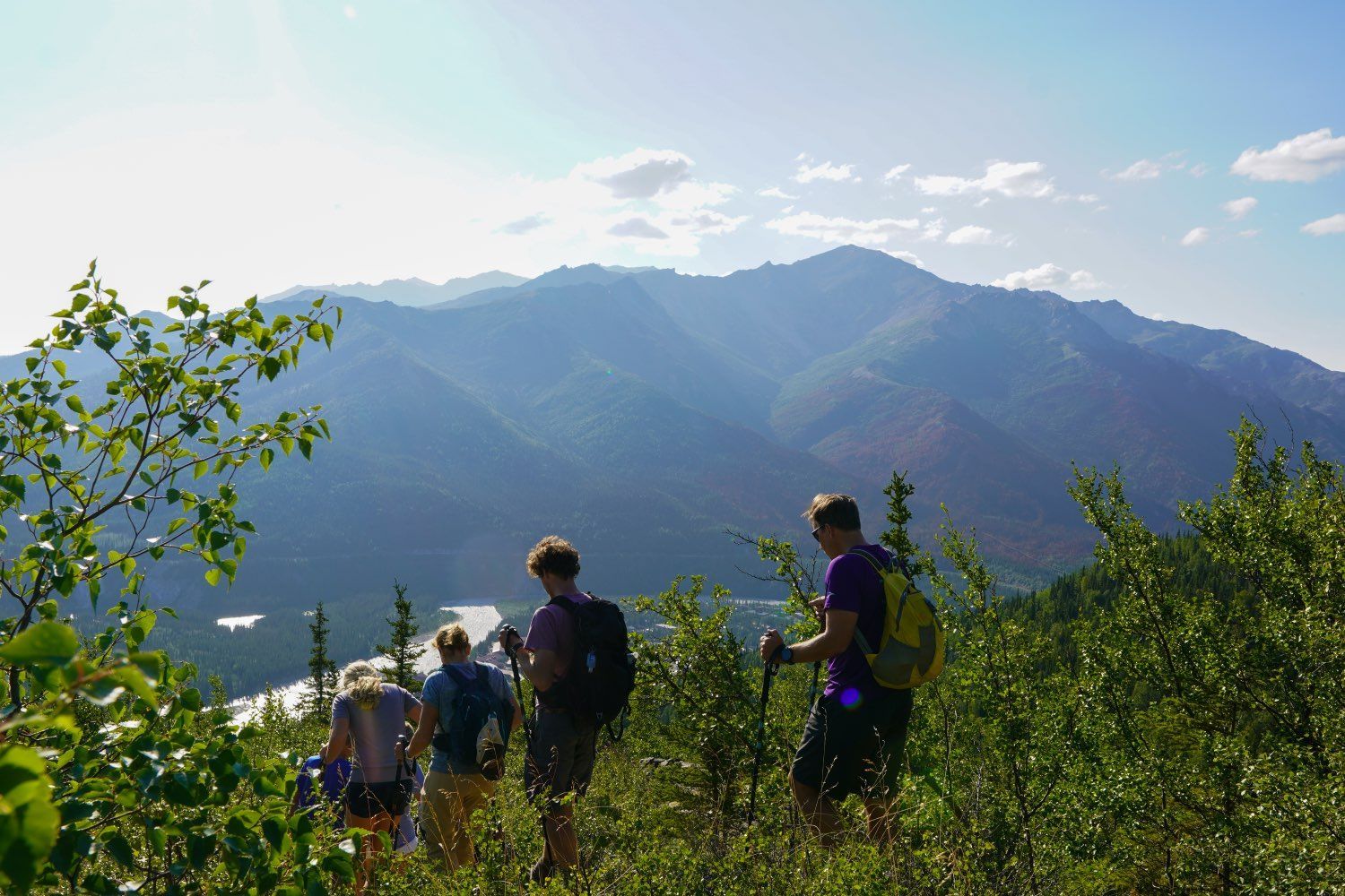 Hikers on a grassy mountain overlook with sunlit blue peaks and sky in the background