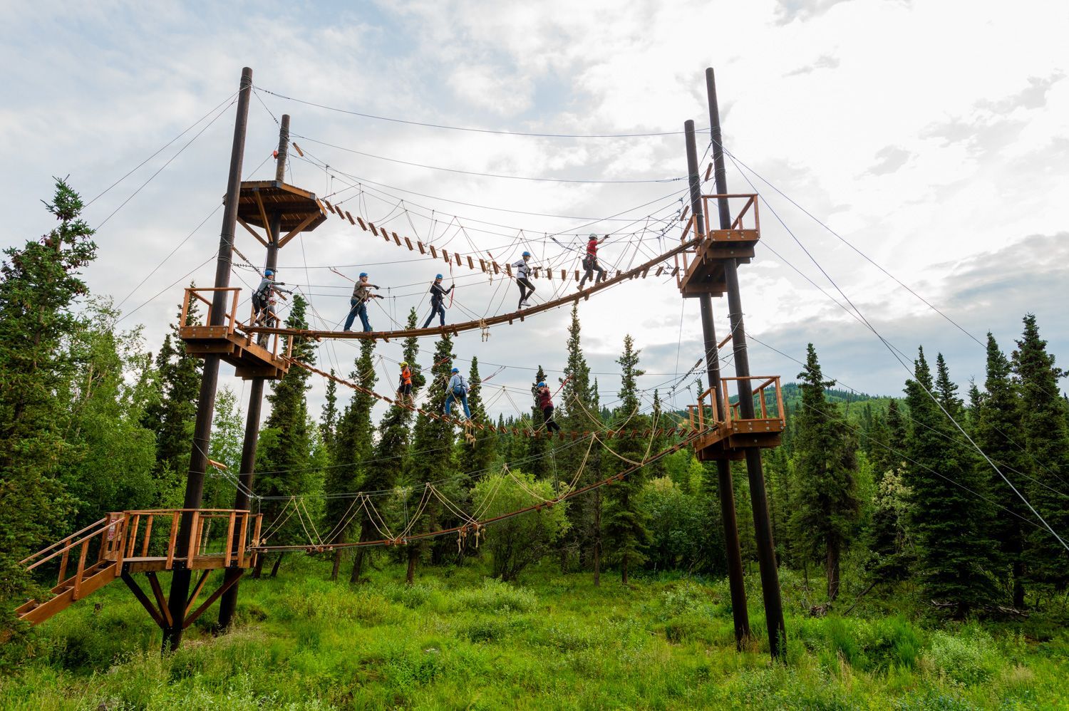Ropes course with suspended bridges and platforms in a forest clearing under a cloudy sky