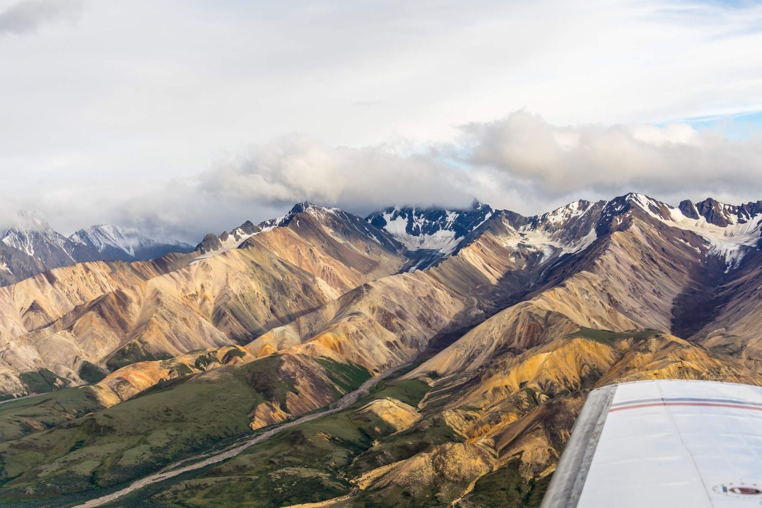 Snowy mountain range viewed from an airplane wing under cloudy skies