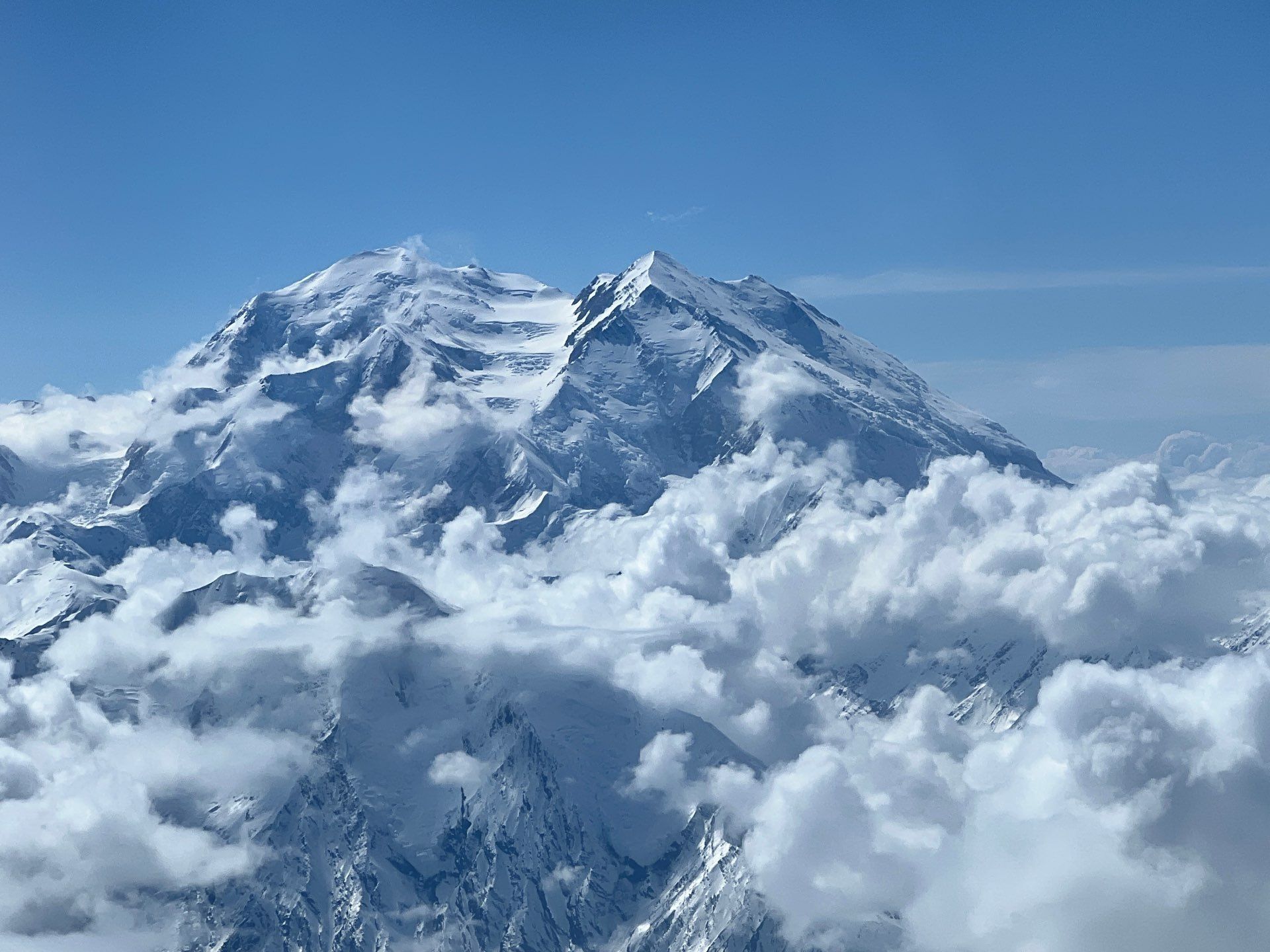 Snow-covered mountain peak rising above clouds under a clear blue sky