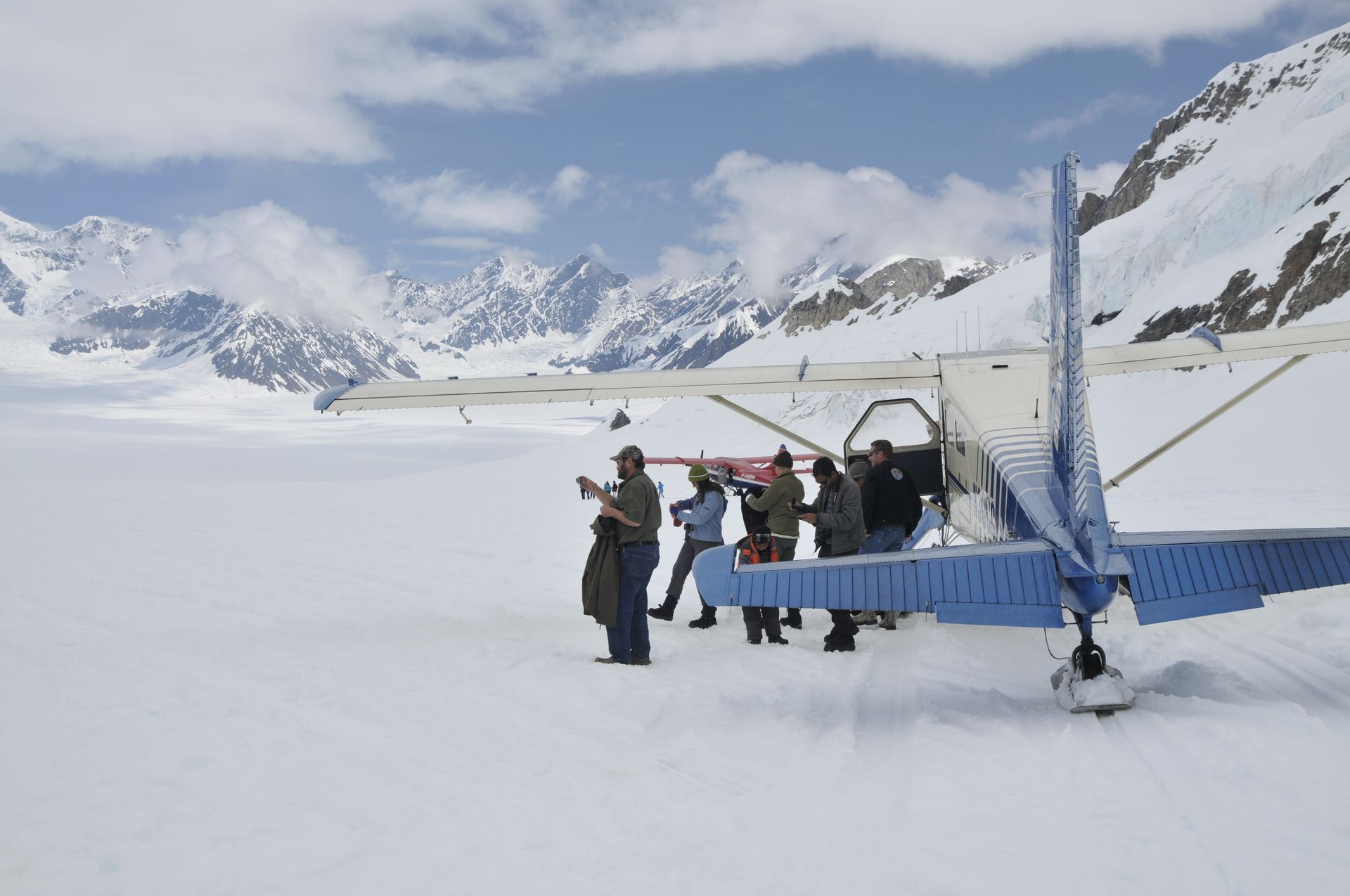 Tourist standing by a blue aircraft on a snowy airfield with mountains