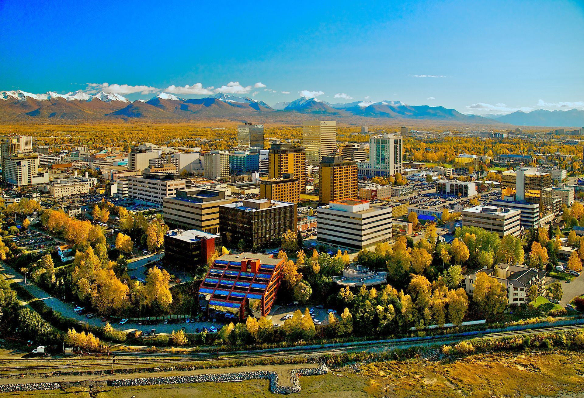 City skyline with autumn trees and snowy mountains in the background