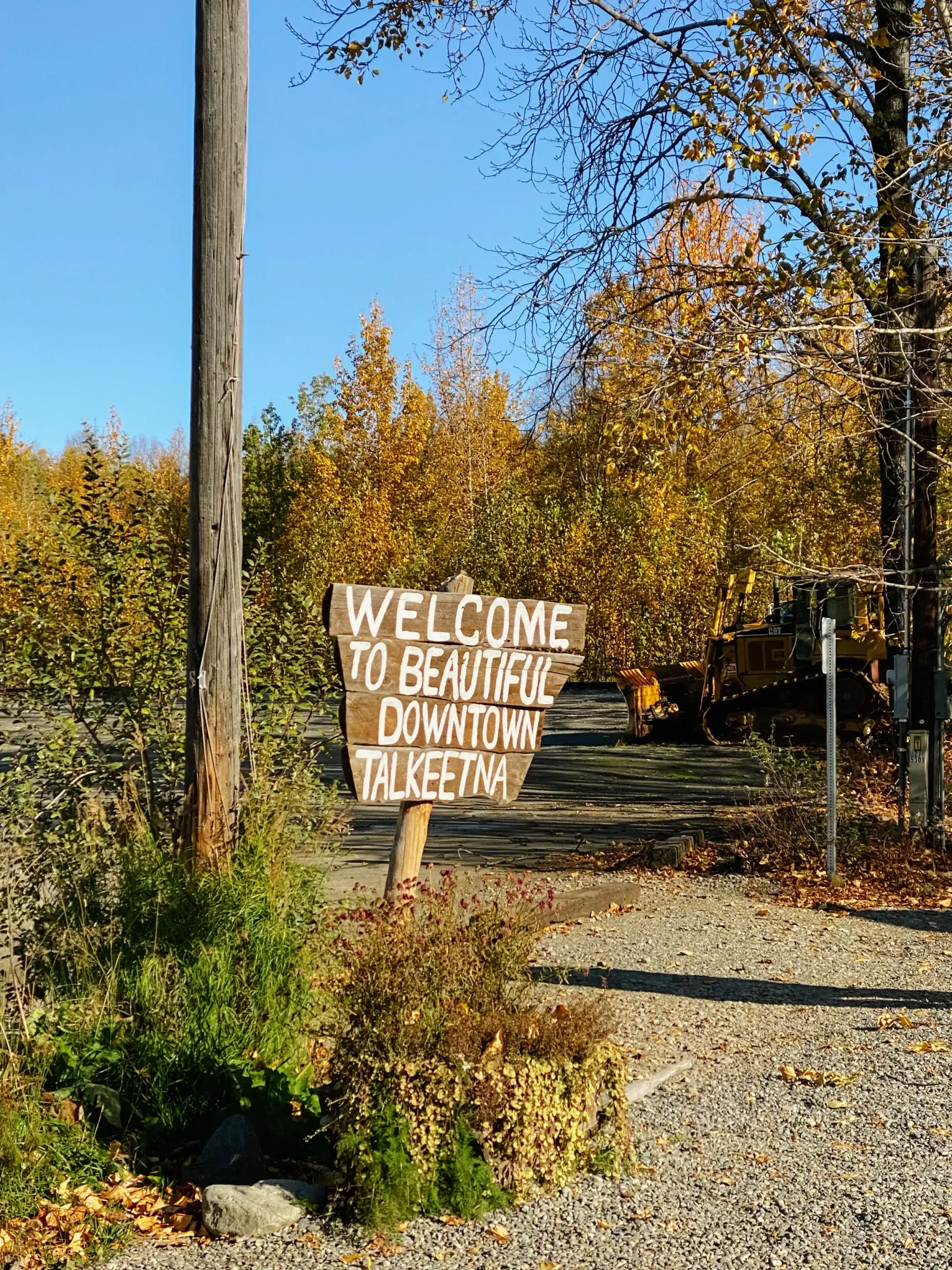 Hand-painted welcome sign beside a gravel path in a wooded autumn setting