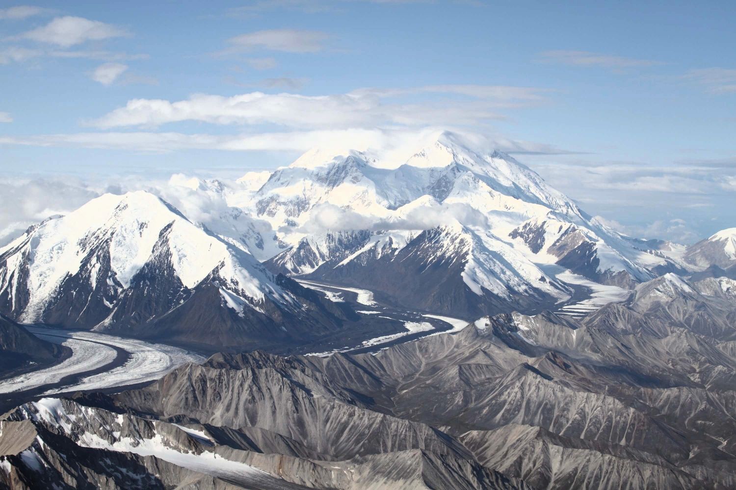 Snow-covered mountain range under a blue sky, with rugged dark foothills in the foreground