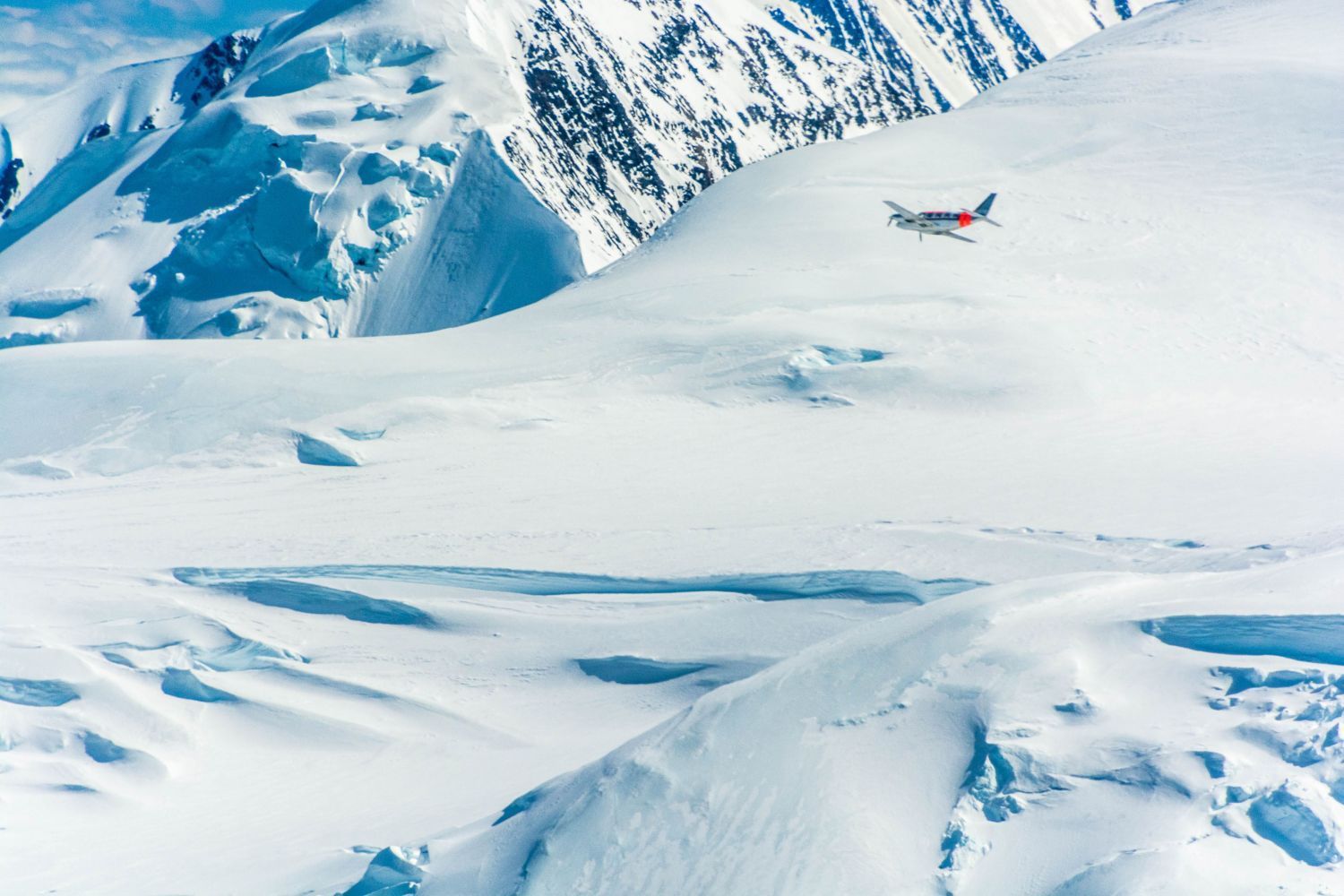 Tiny plane flying over a snowy mountain landscape