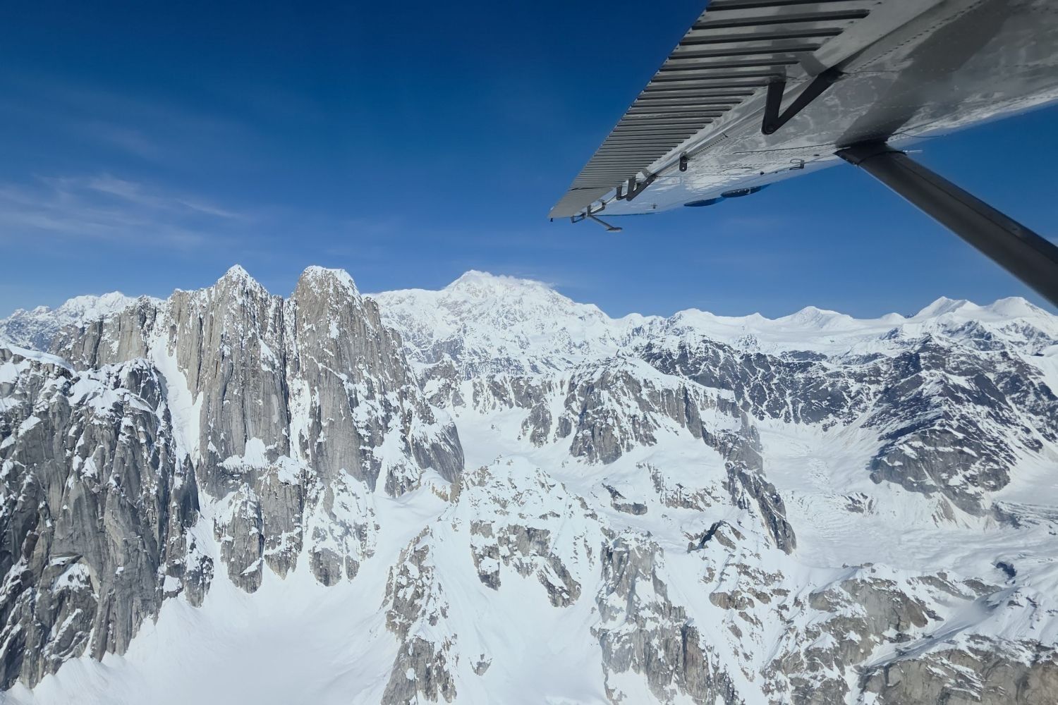 Snowy mountain peaks under a clear blue sky, seen from an aircraft wing.