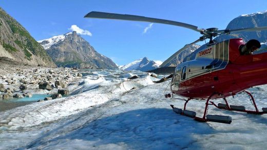 Red helicopter on snowy mountain landing near glacier under clear blue sky