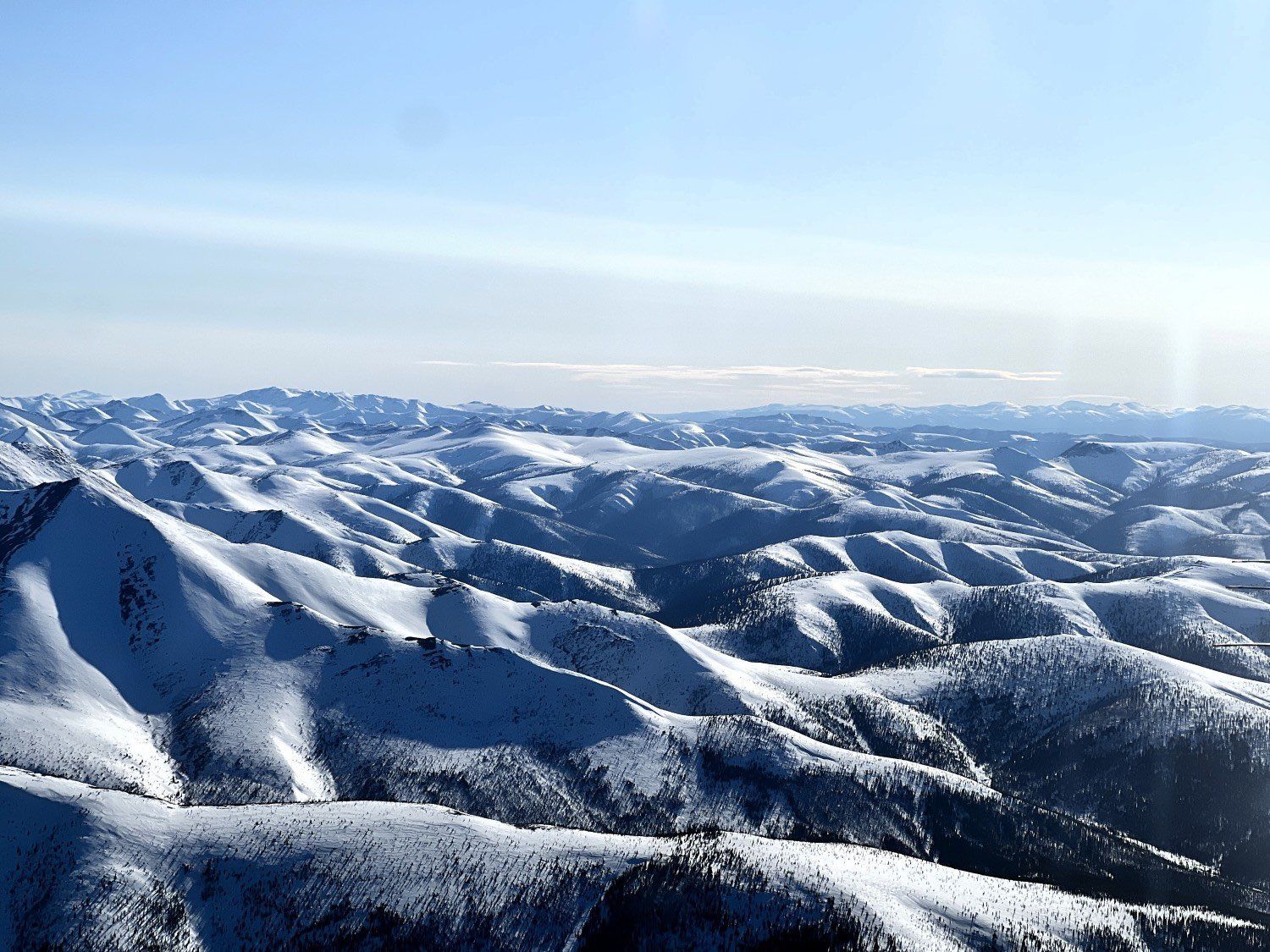 Snow-covered mountain ridges under a clear blue sky, with distant peaks on the horizon