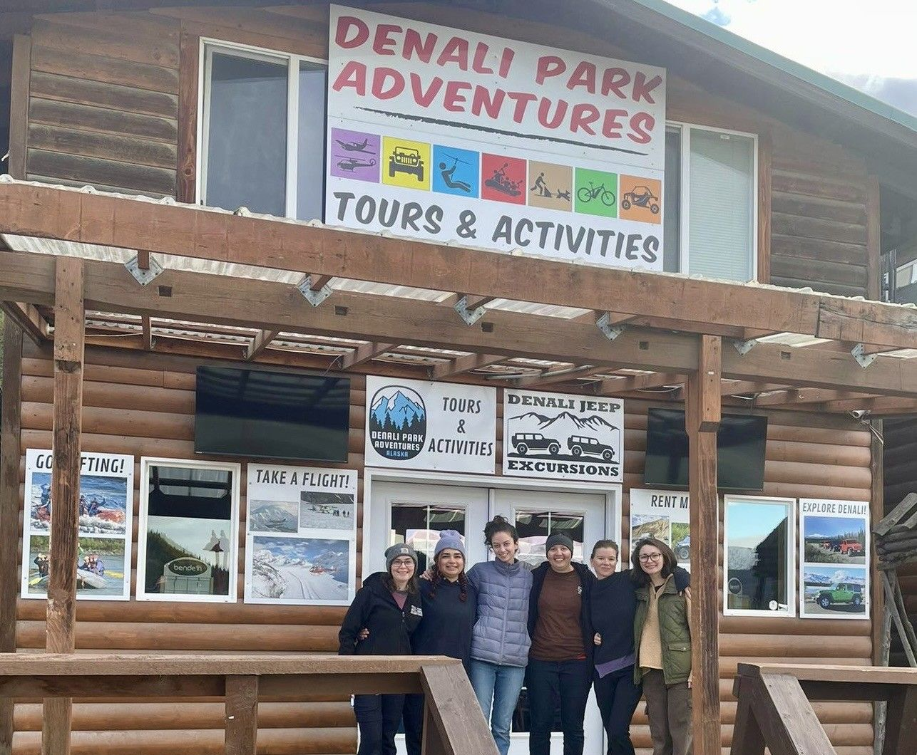 Group posing in front of Denali Park Adventures tour and activities cabin sign