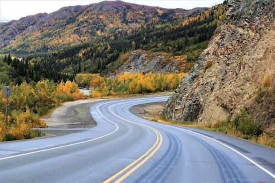 Winding paved road through autumn mountains beside a rocky cliff under a clear sky