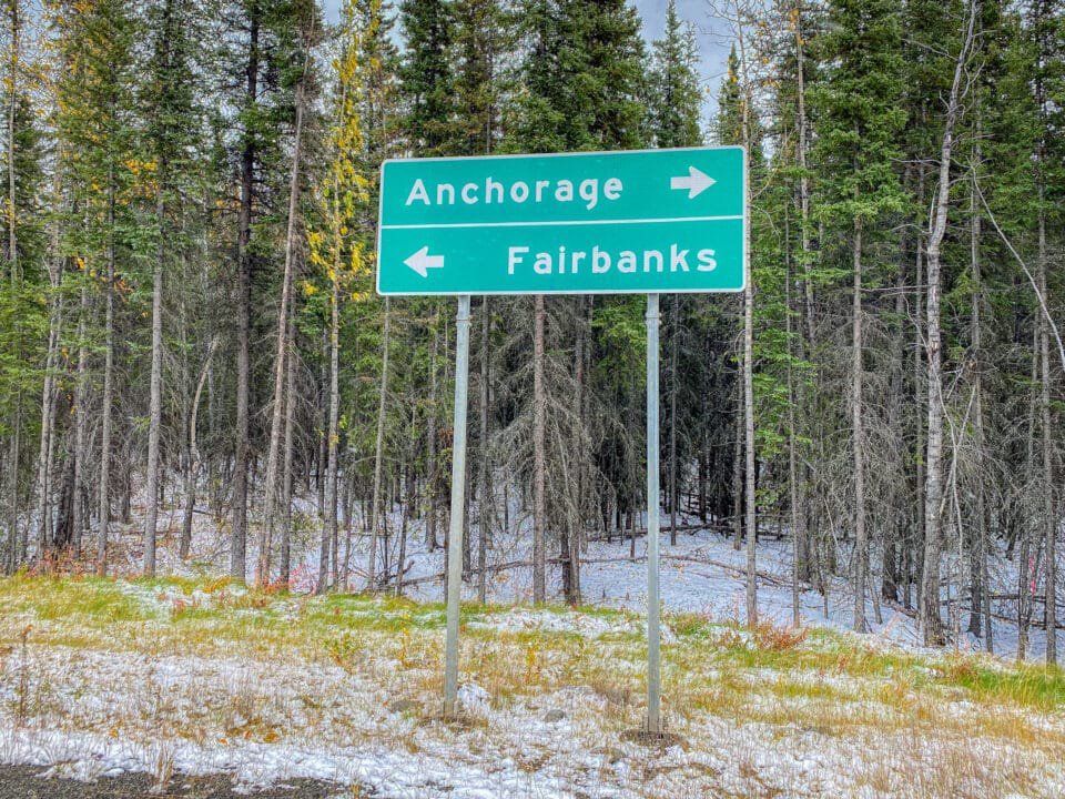 Road sign in a snowy forest points to Anchorage right and Fairbanks left.