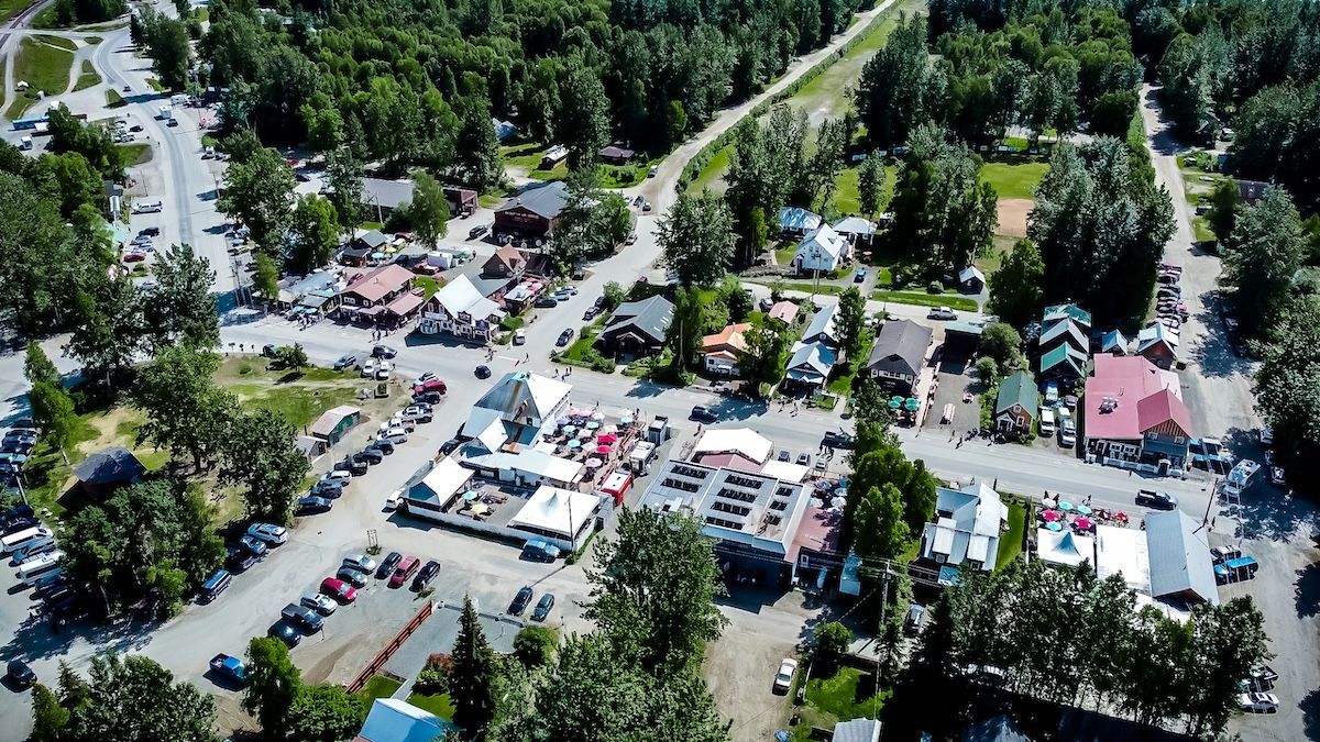 Aerial view of a crowded outdoor fair with tents, parked cars, and trees along a road.