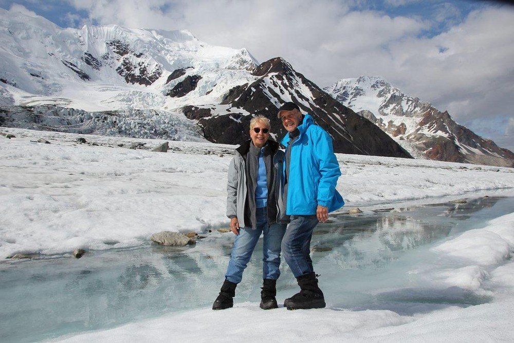 Two people standing on a snowy glacier with mountains in the background