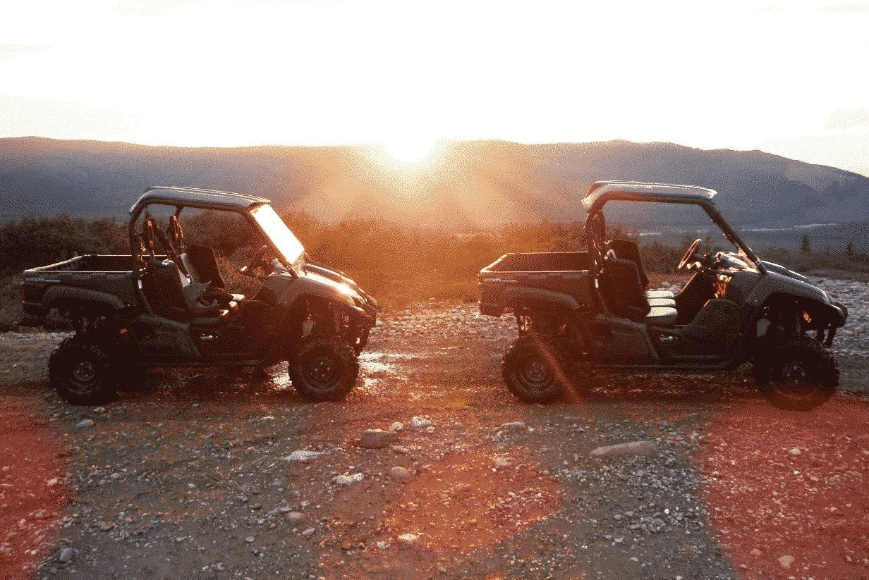 Two off-road buggies parked on a gravel road at sunset with hills in the background
