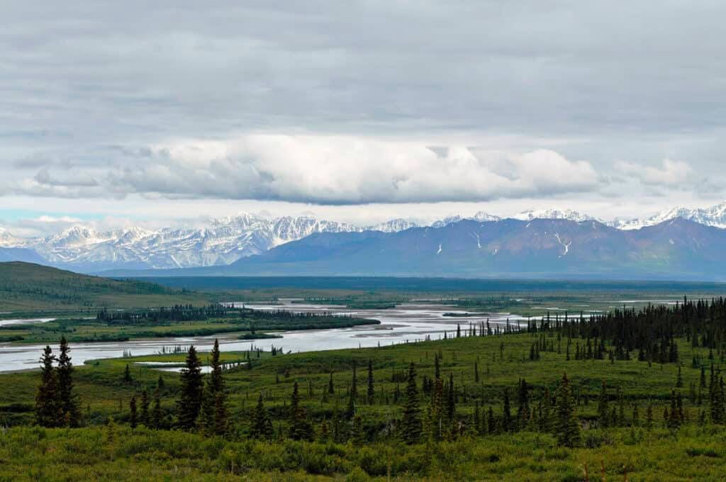 Snow-capped mountains above a winding river and green valley under a cloudy sky