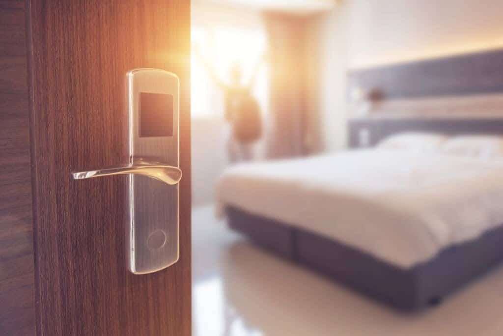 Hotel room door with a lit brass handle, bedroom blurred in the background