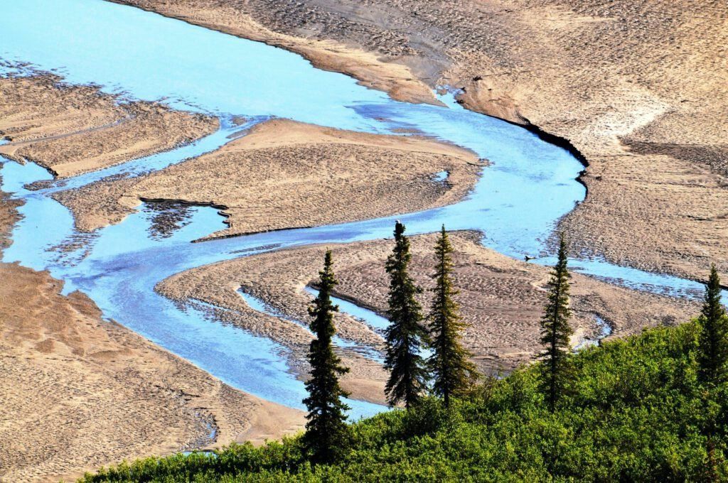 Blue river winding through a dry, rocky landscape with green trees in the foreground.