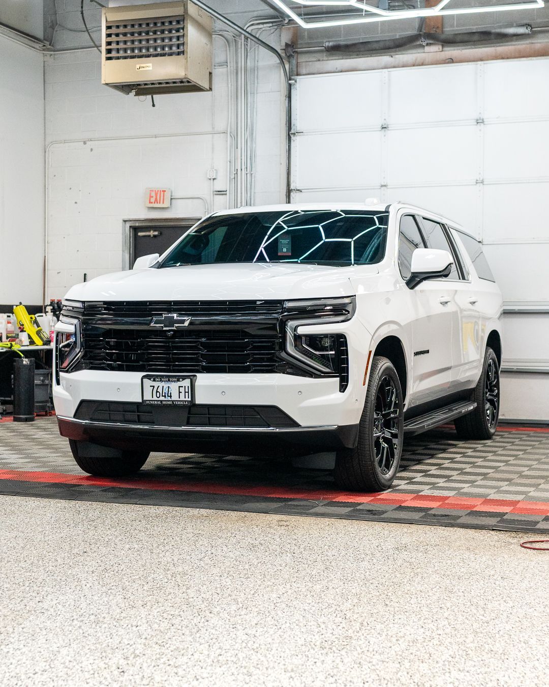 White SUV parked indoors in a garage, front view with black grille and tinted windows.