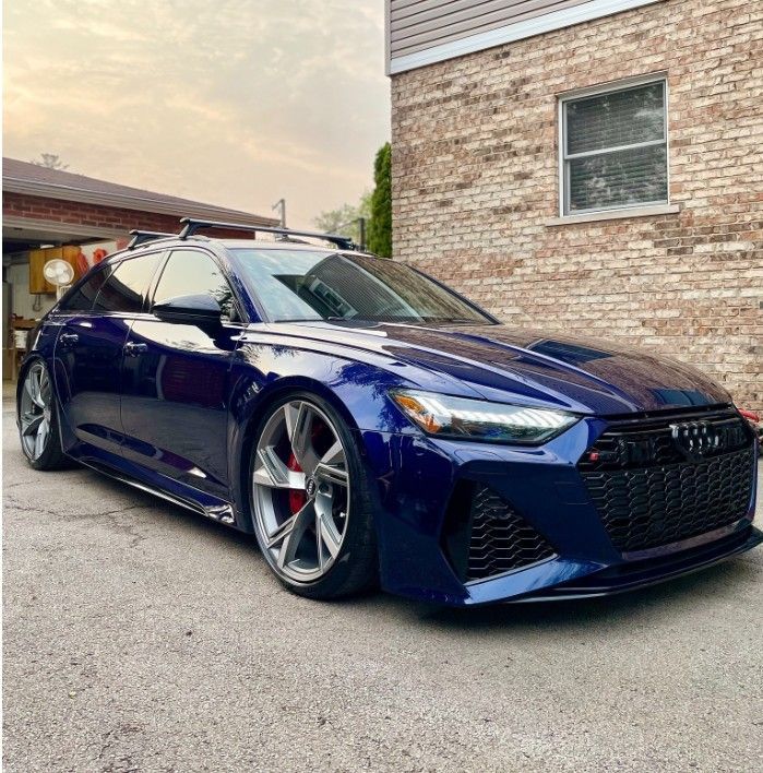 Blue sports sedan parked beside a brick house at dusk