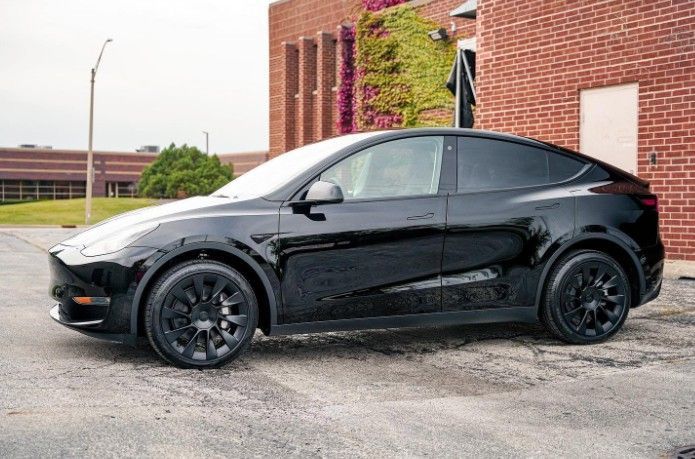 Black Tesla Model Y parked beside a brick building on a wet lot