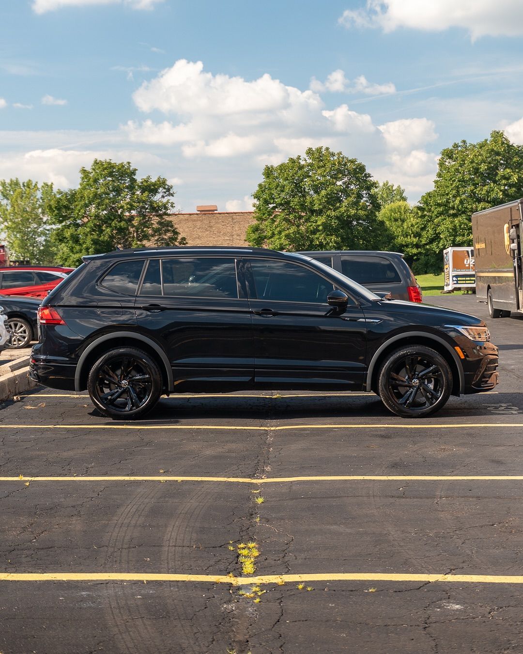 Black SUV parked in a lot under a partly cloudy sky, side view