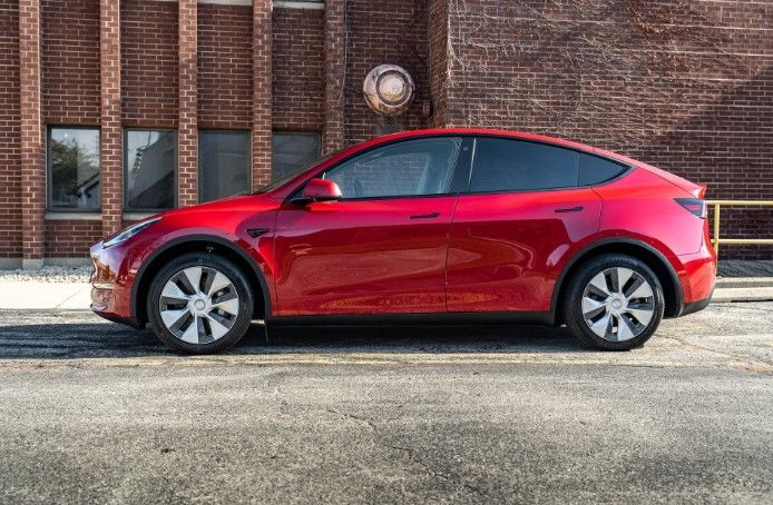 Red Tesla Model 3 parked beside a brick building in daylight